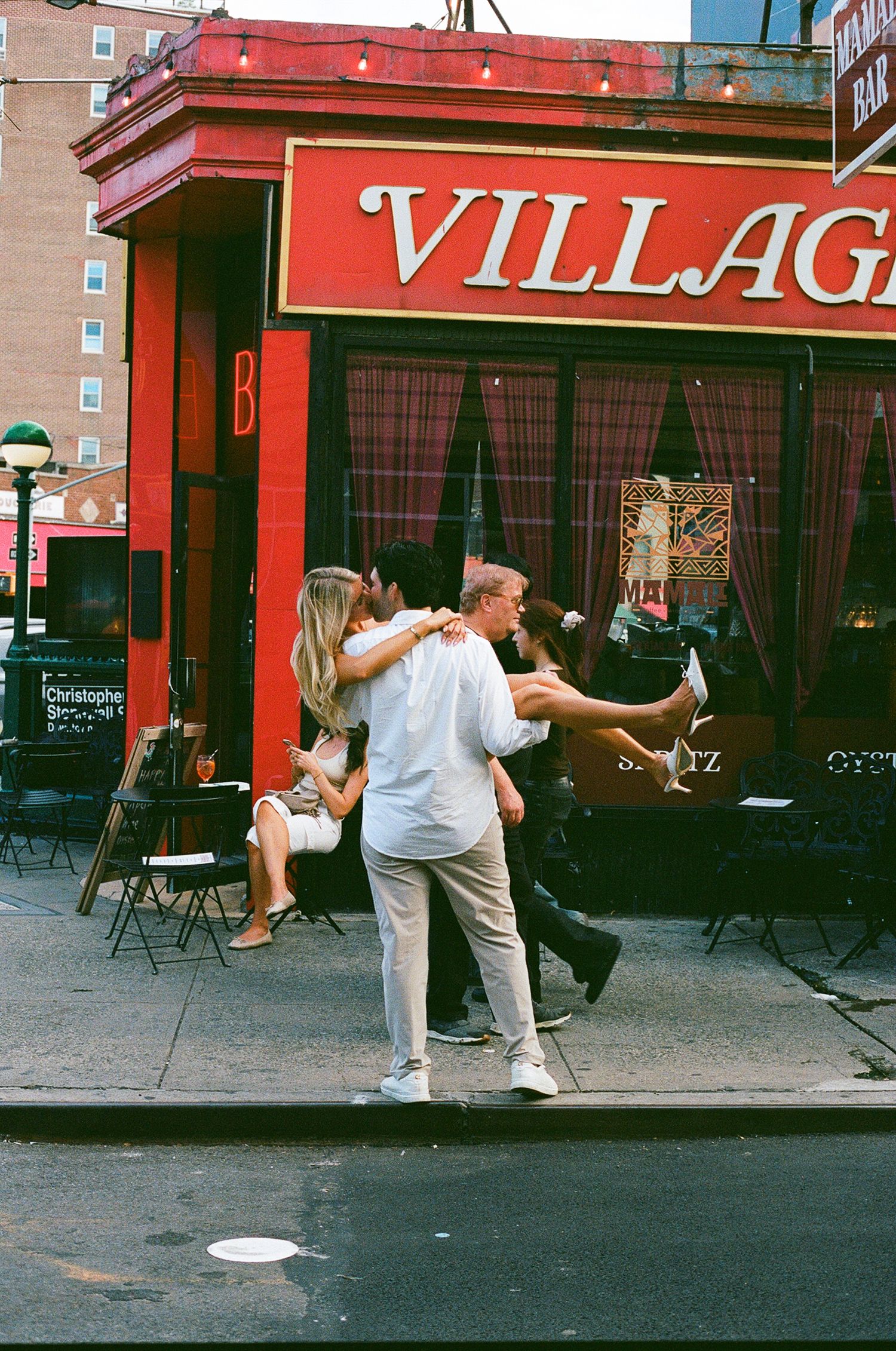 A couple dances playfully outside a red Village restaurant on a city street corner.