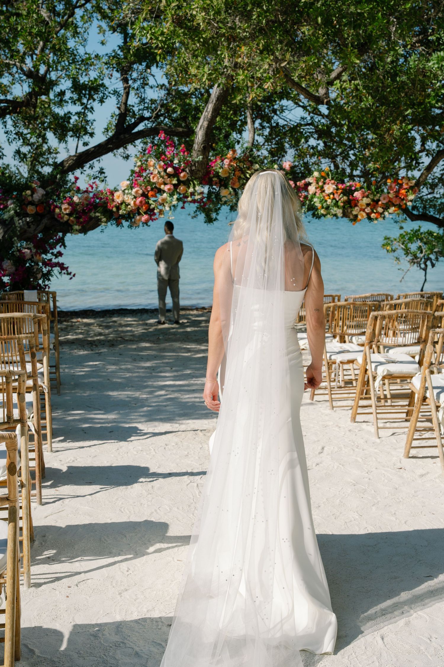 Beach wedding setup with white chairs and floral arrangements on a sandy shore.
