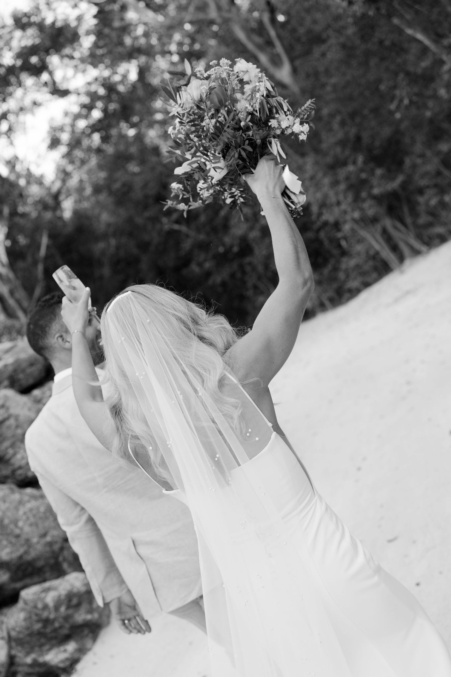 Black and white photo of wedding party in flowing white dresses against natural backdrop.
