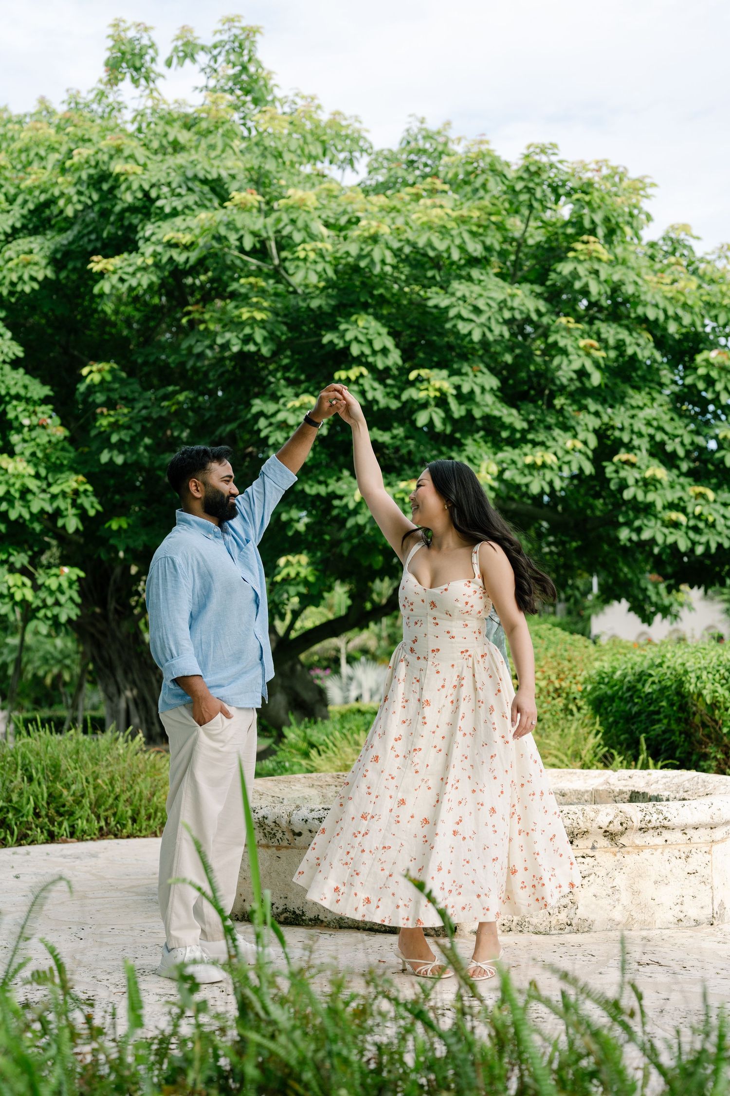 Couple dancing outdoors in a lush green garden, man in blue shirt and woman in floral dress.