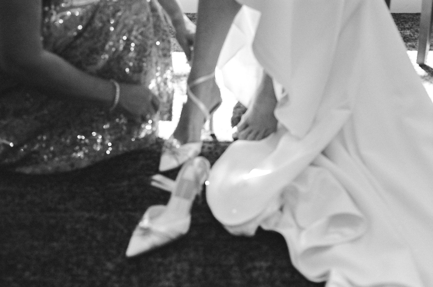 Close-up black and white shot of someone helping with bridal shoes.