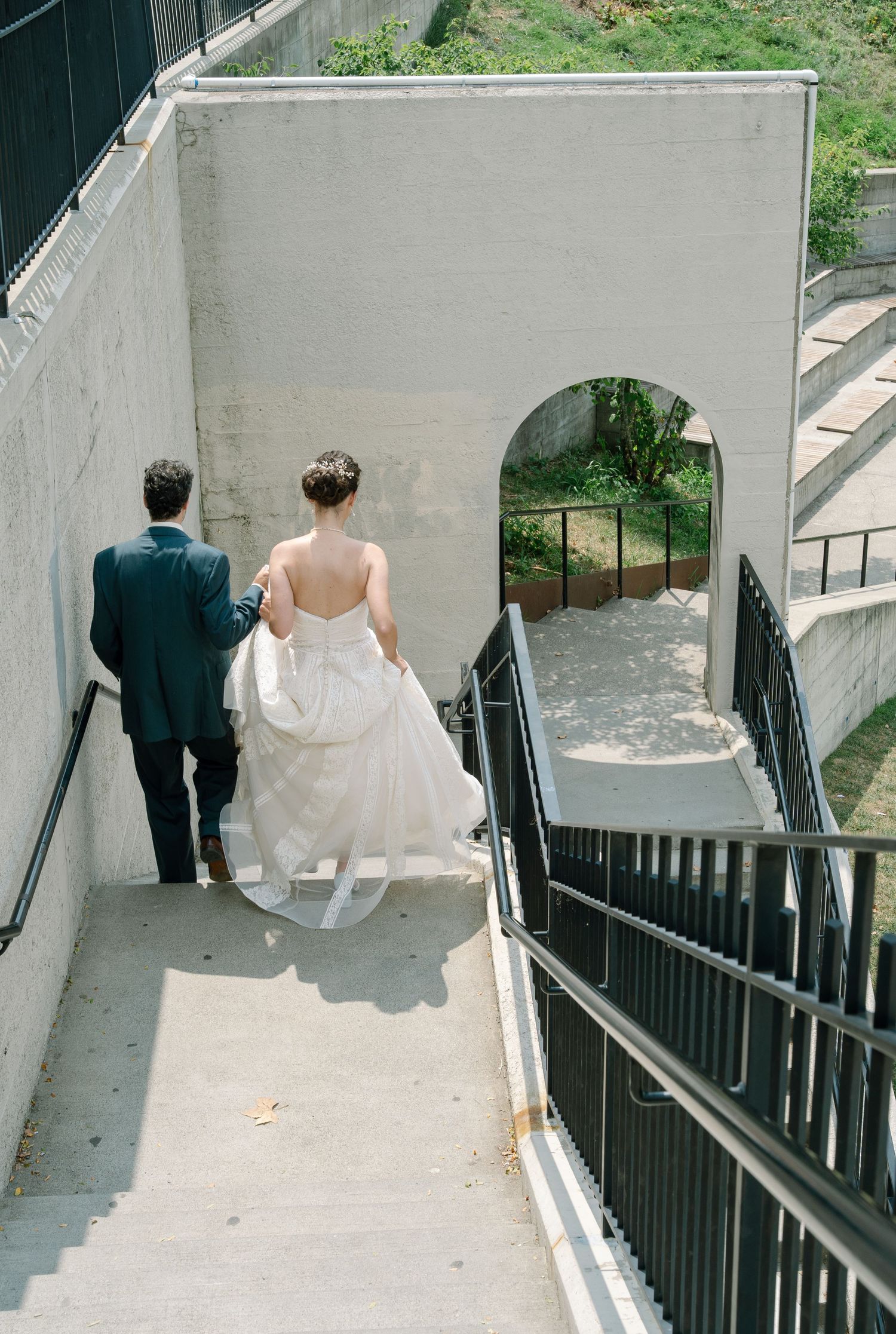 A couple descends white concrete stairs together at their wedding.