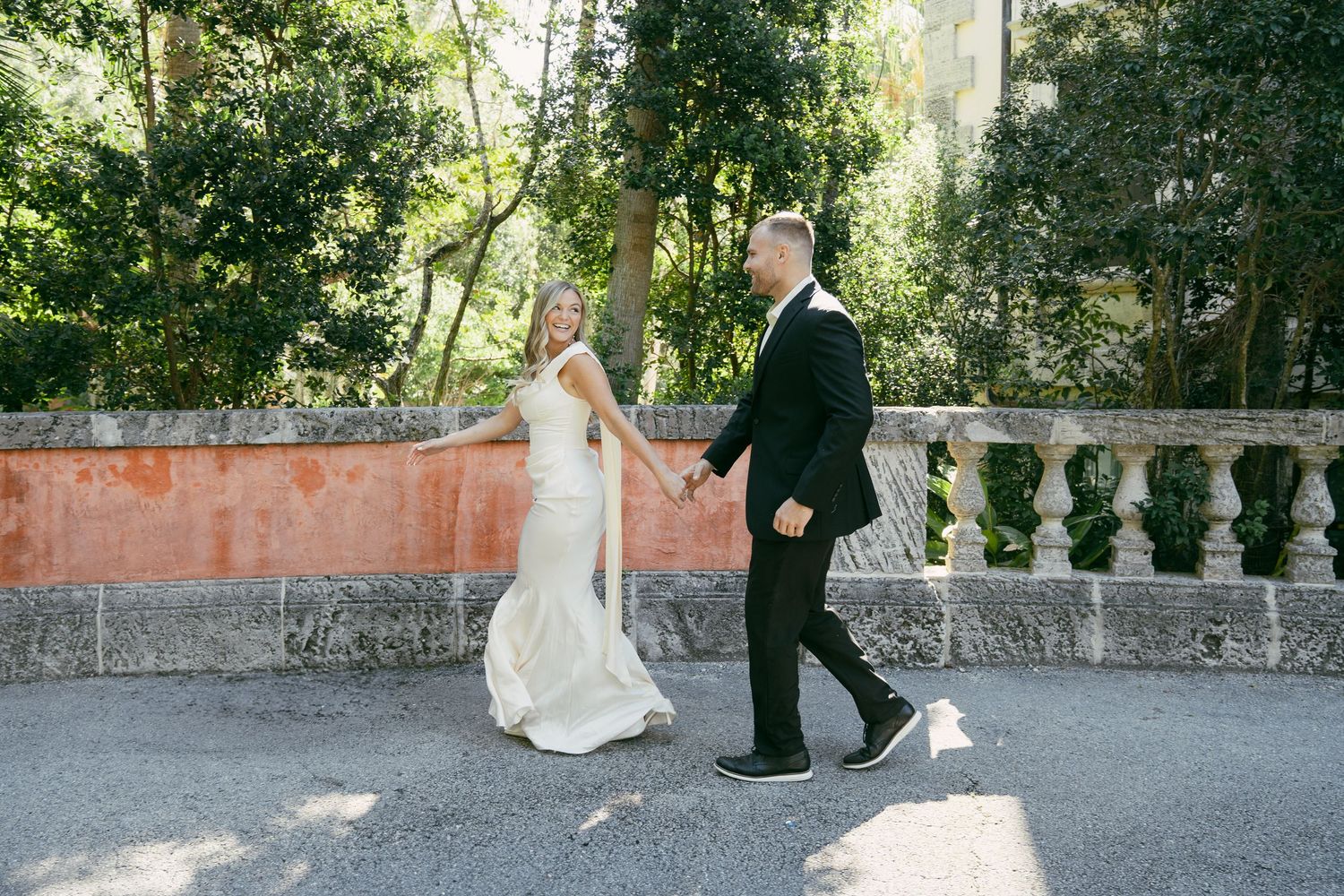 Two people walk together on a stone path surrounded by lush greenery on a sunny afternoon.