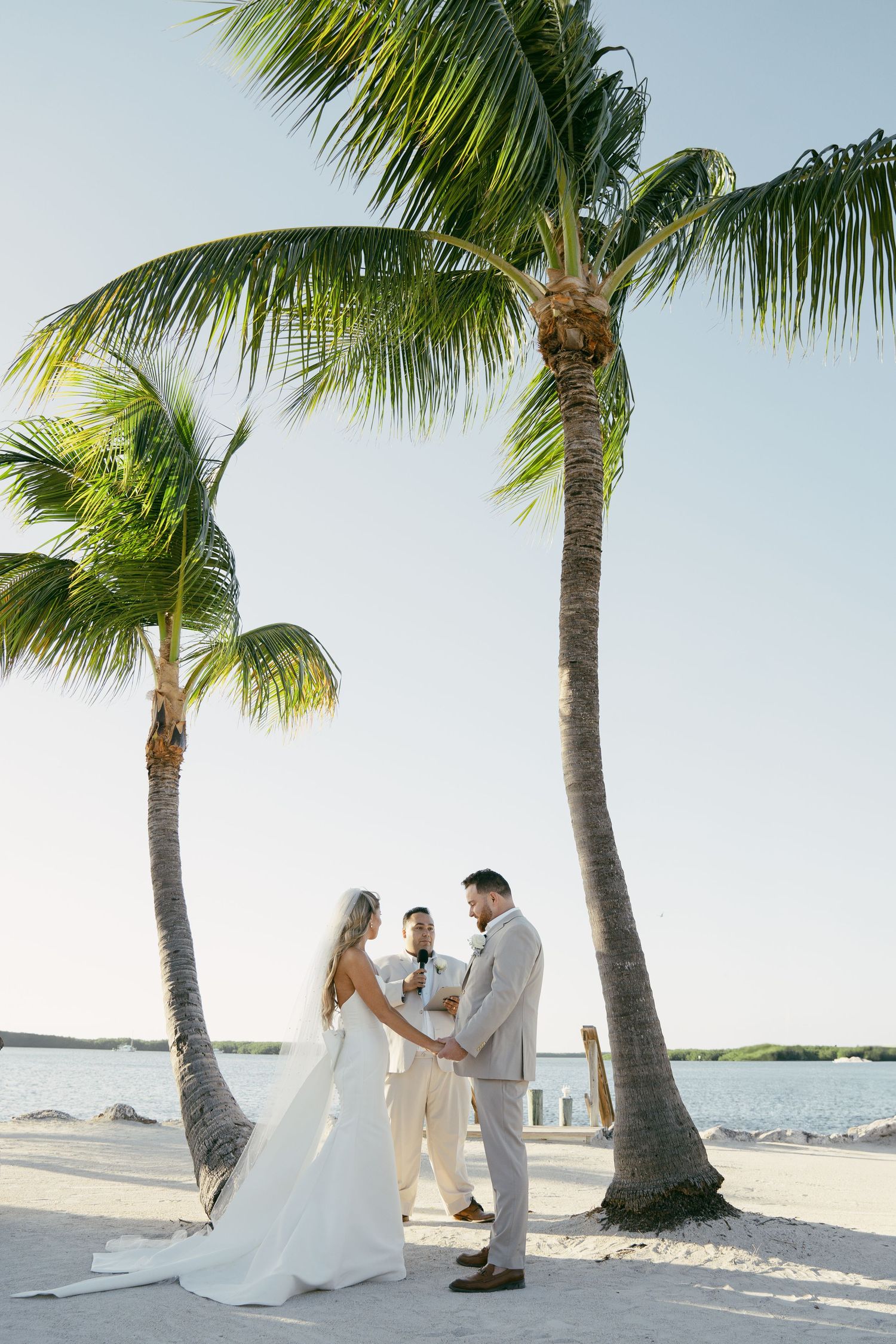 Newlywed couple shares romantic moments on a tropical beach with palm trees and white sand.