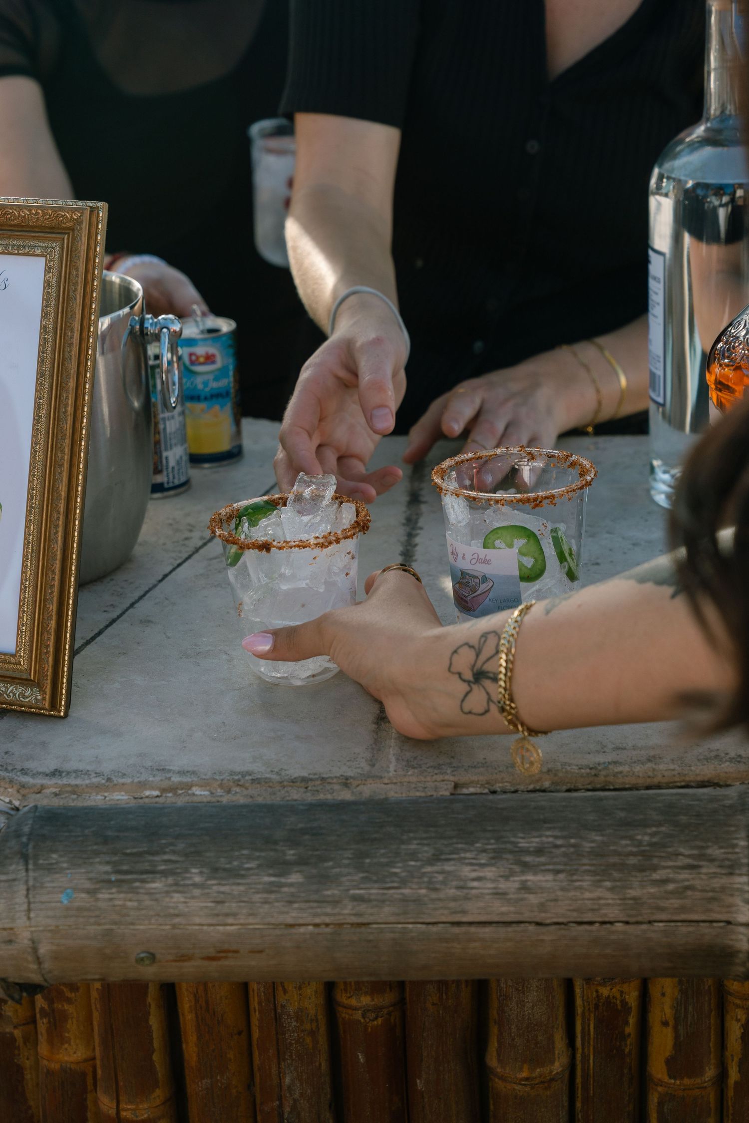 Bartender serving two salted rim cocktail glasses with lime garnish on a rustic wooden bar counter.