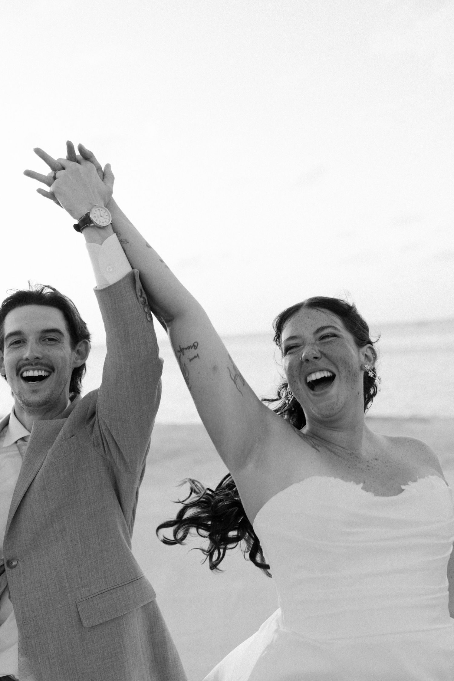 A couple laugh and raise their arms in celebration on a beach.
