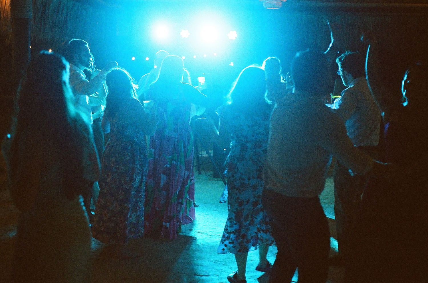 An image of a group of people, likely at a wedding reception, dancing and celebrating together in a dimly lit venue.