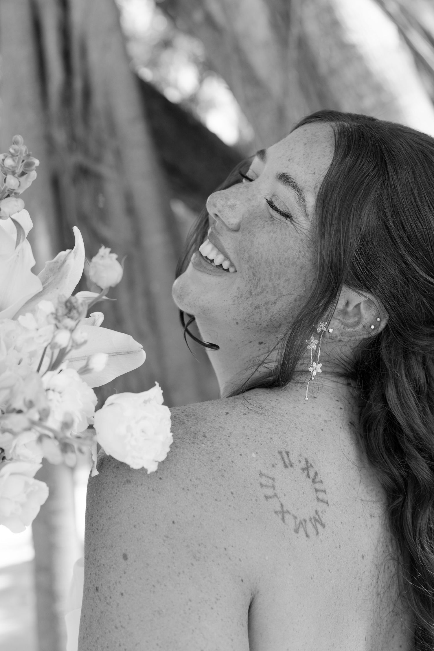 A woman with long dark hair smiling while holding a bouquet of flowers.