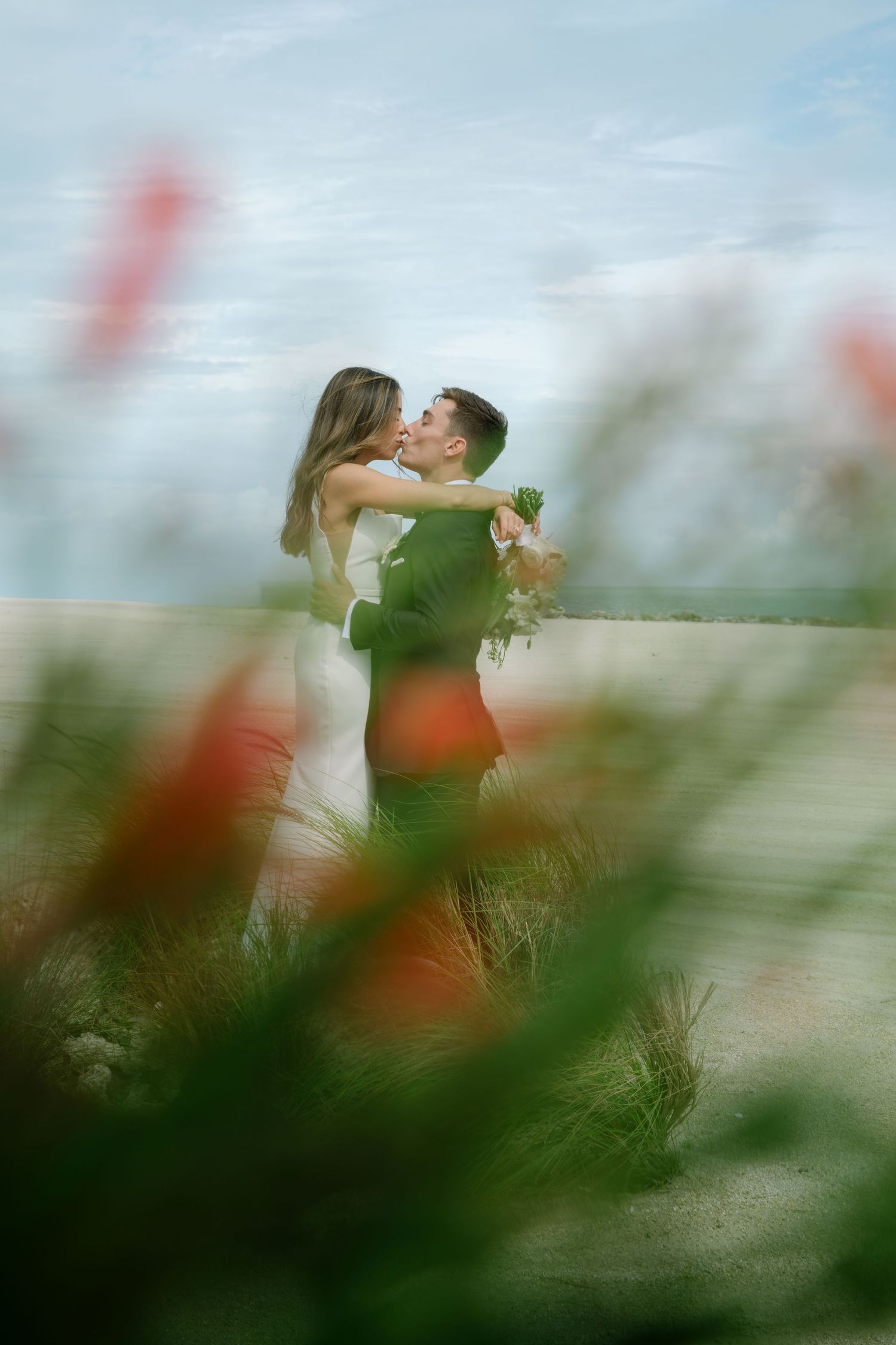 Bride and groom sharing a romantic kiss surrounded by colorful wildflowers in a dreamy outdoor setting.