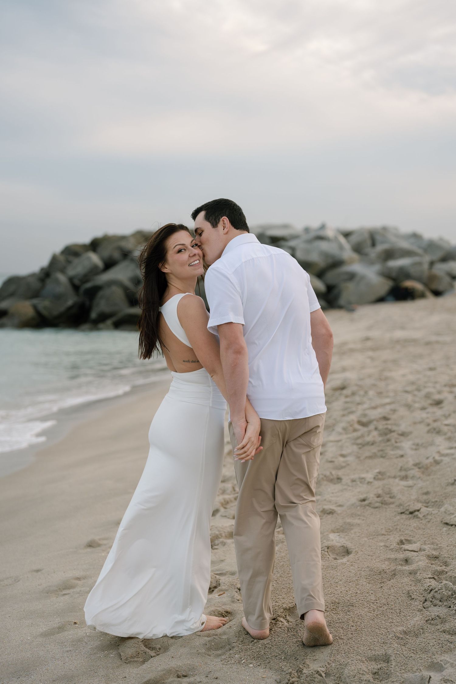 Playful couple's photoshoot sequence on sandy beach with rock formations.