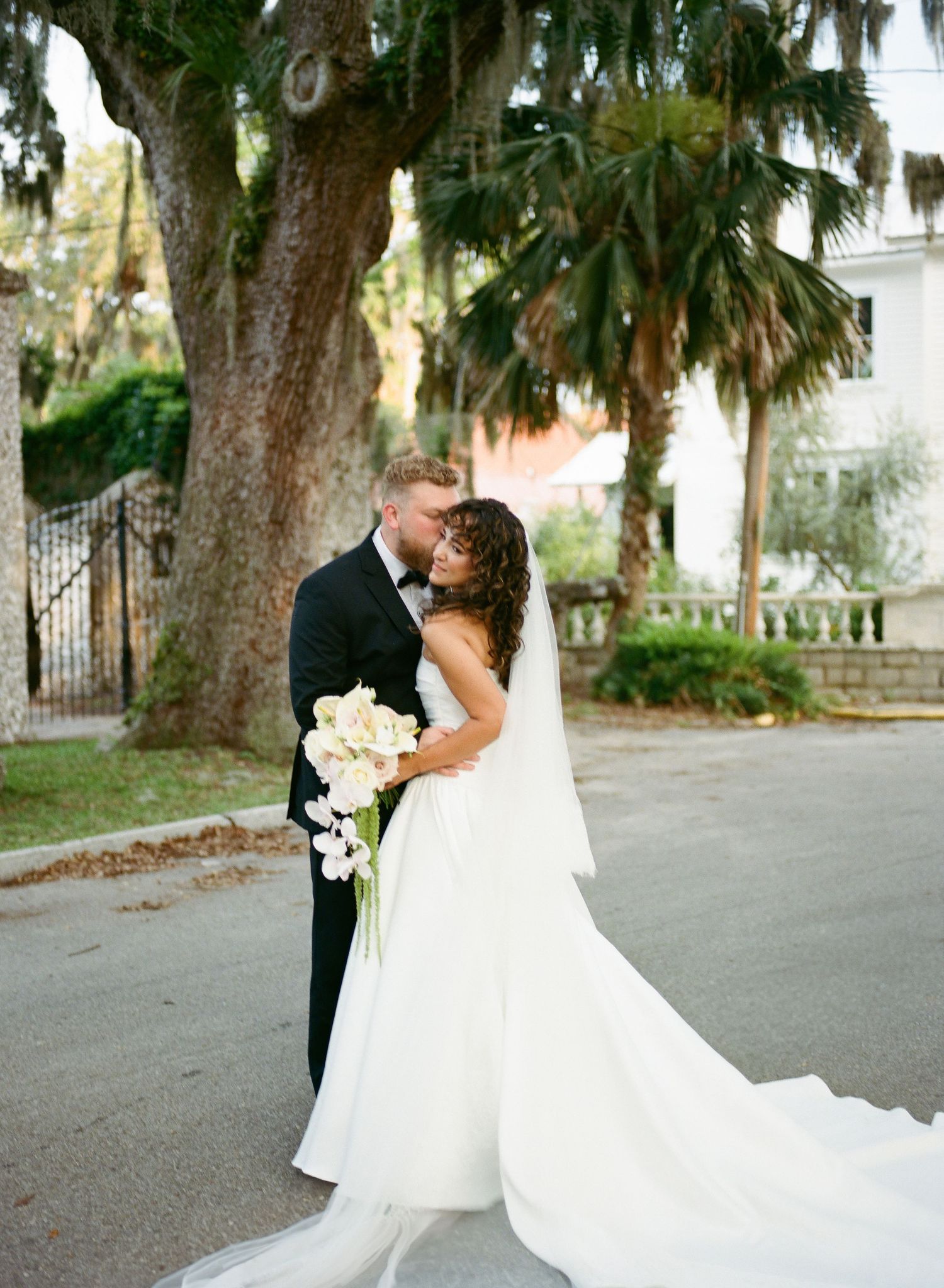 Romantic wedding couple embraces under palm trees and Spanish moss on a Charleston street.