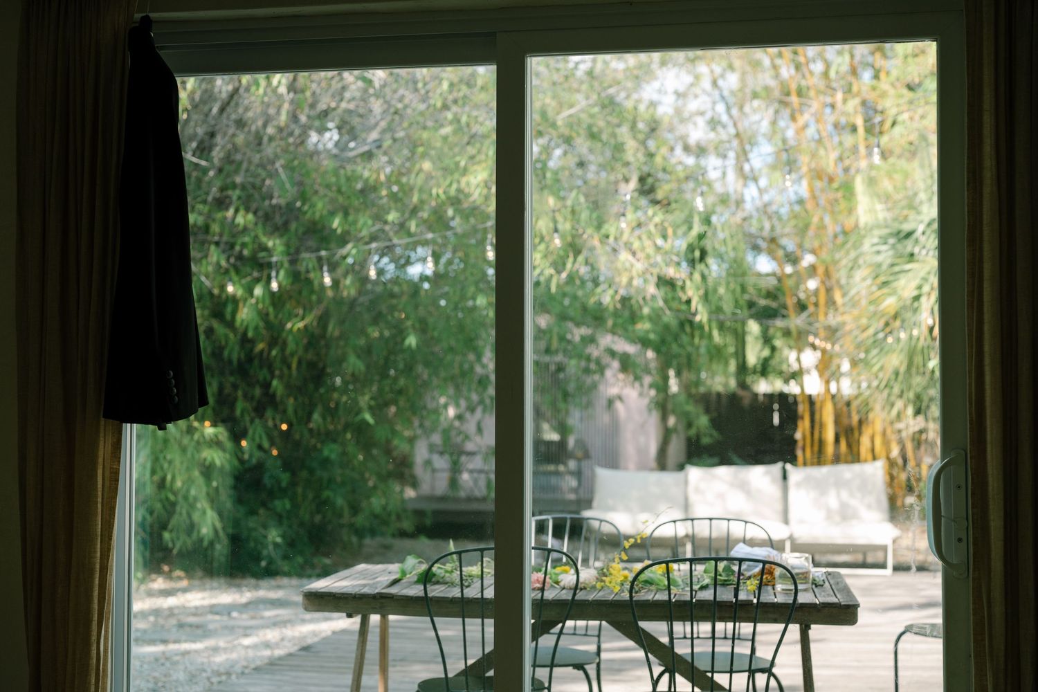 A modern sunroom with large windows overlooking a lush backyard garden and patio furniture.
