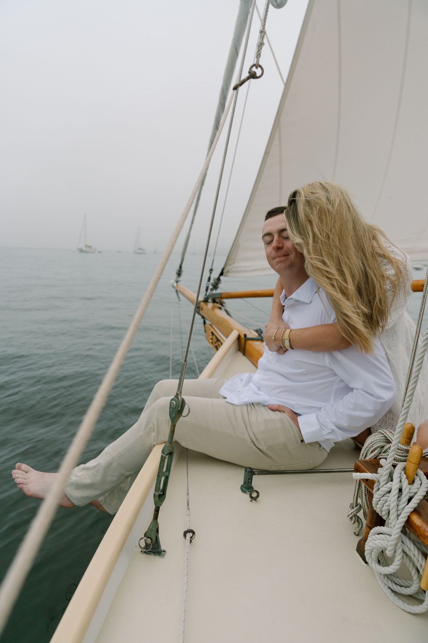 Couple relaxing together on a sailboat deck, surrounded by misty ocean waters on a foggy day.