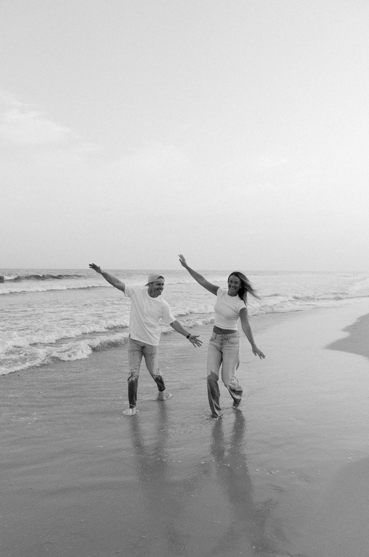 Family walking hand in hand along a misty beach shoreline in black and white.
