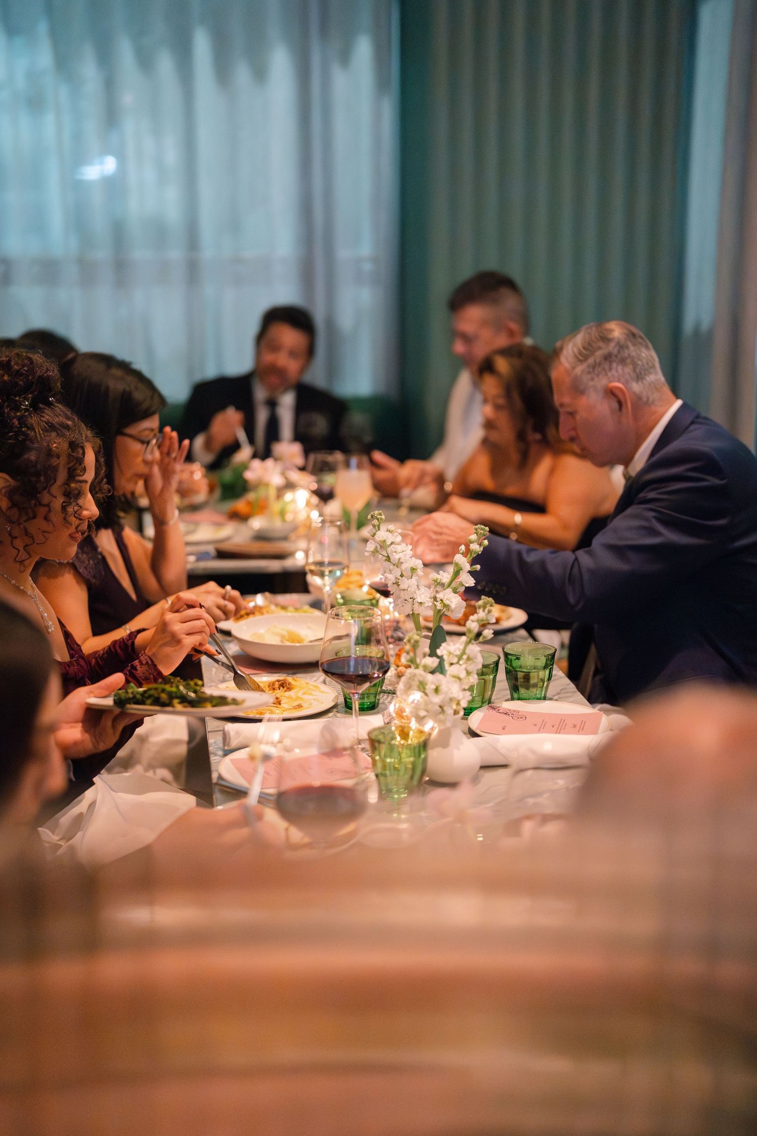 Guests enjoying dinner at long table with green accents and ambient lighting.