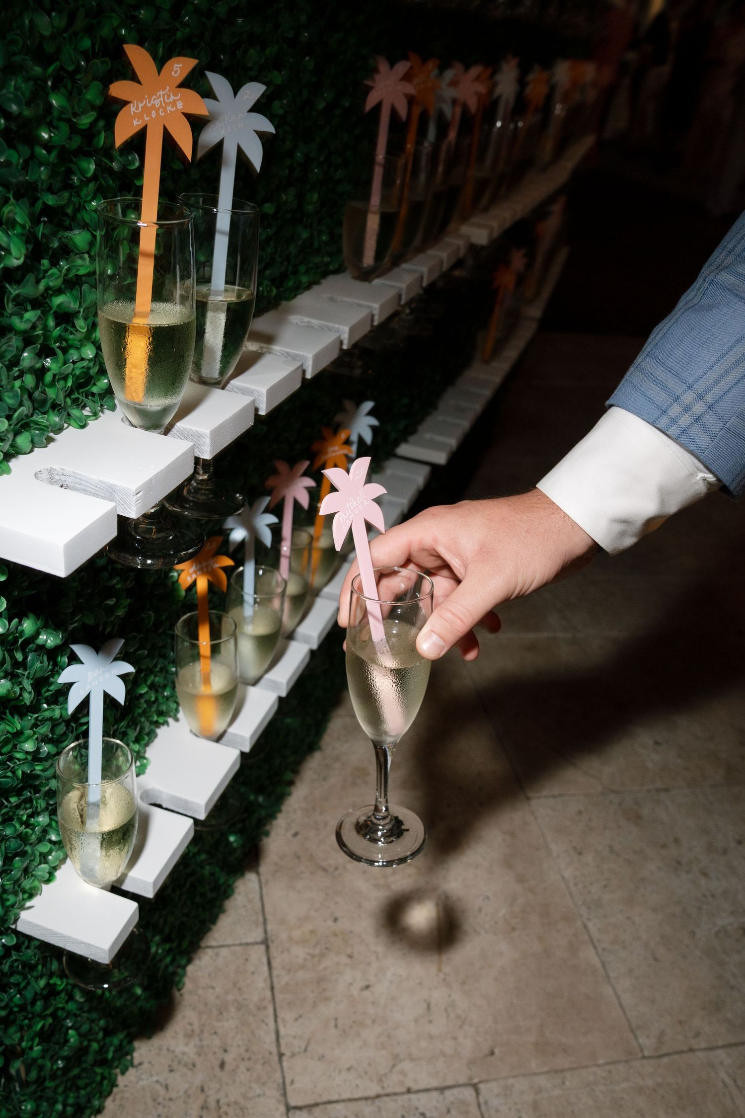 Hand placing decorative palm tree drink stirrer into champagne glass at an elegant party.