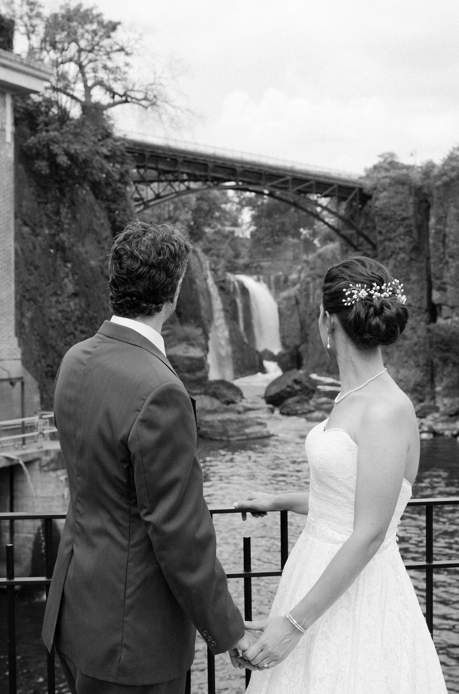 A couple looks out at a scenic waterfall from a viewing platform in black and white imagery.