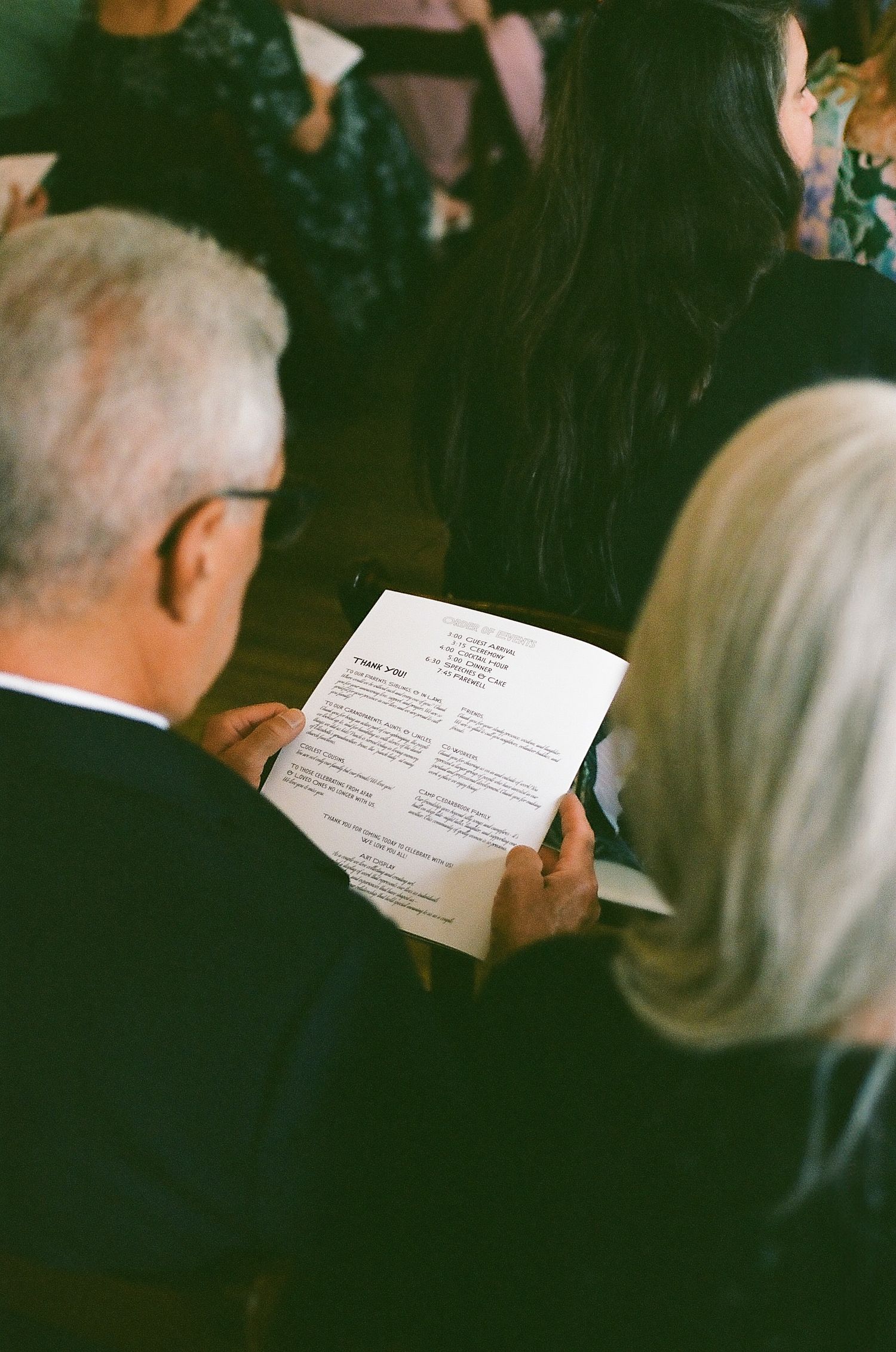 People sitting in dark formal attire reading from papers during an event.