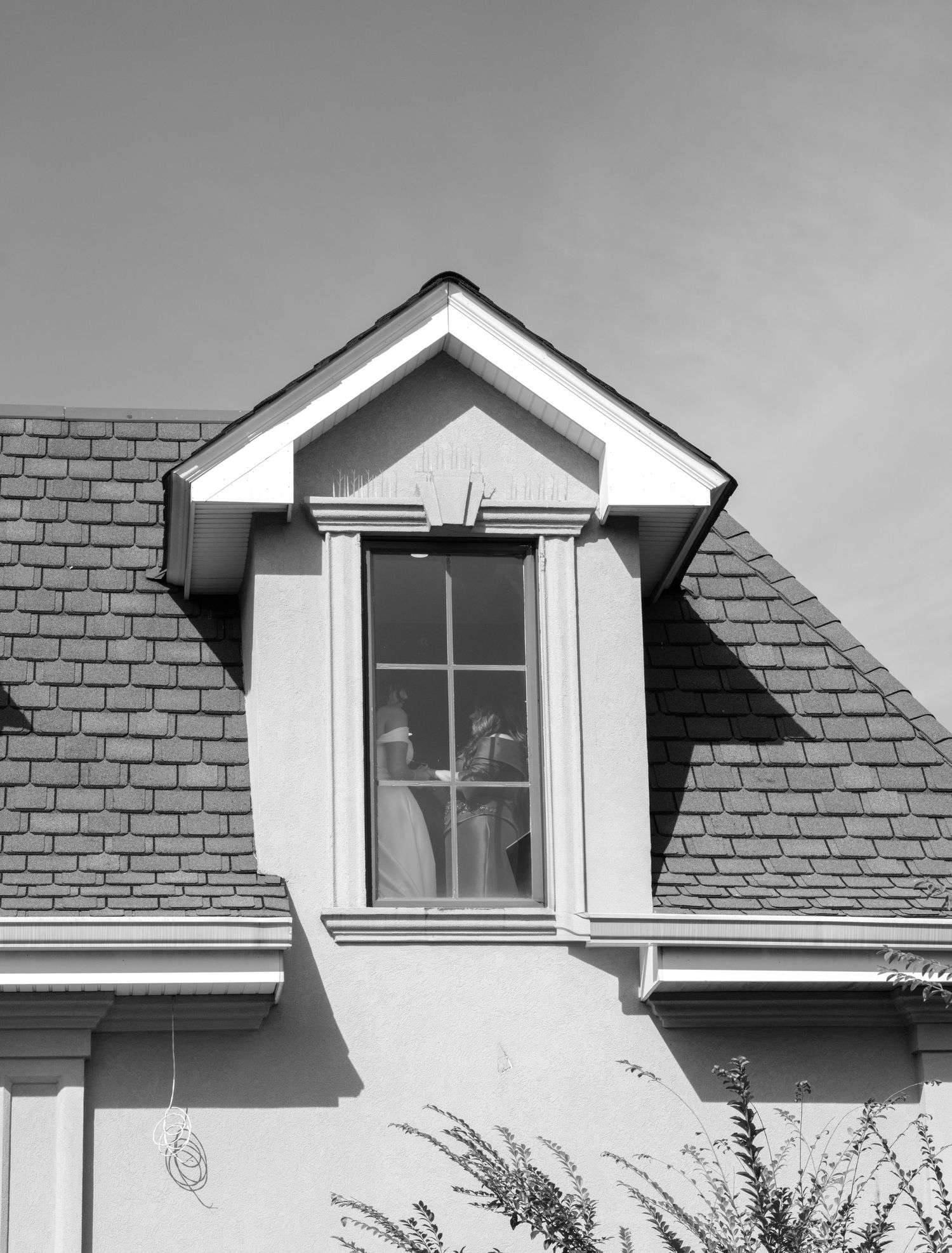 A white dormer window on a brick house casts dramatic shadows in black and white.