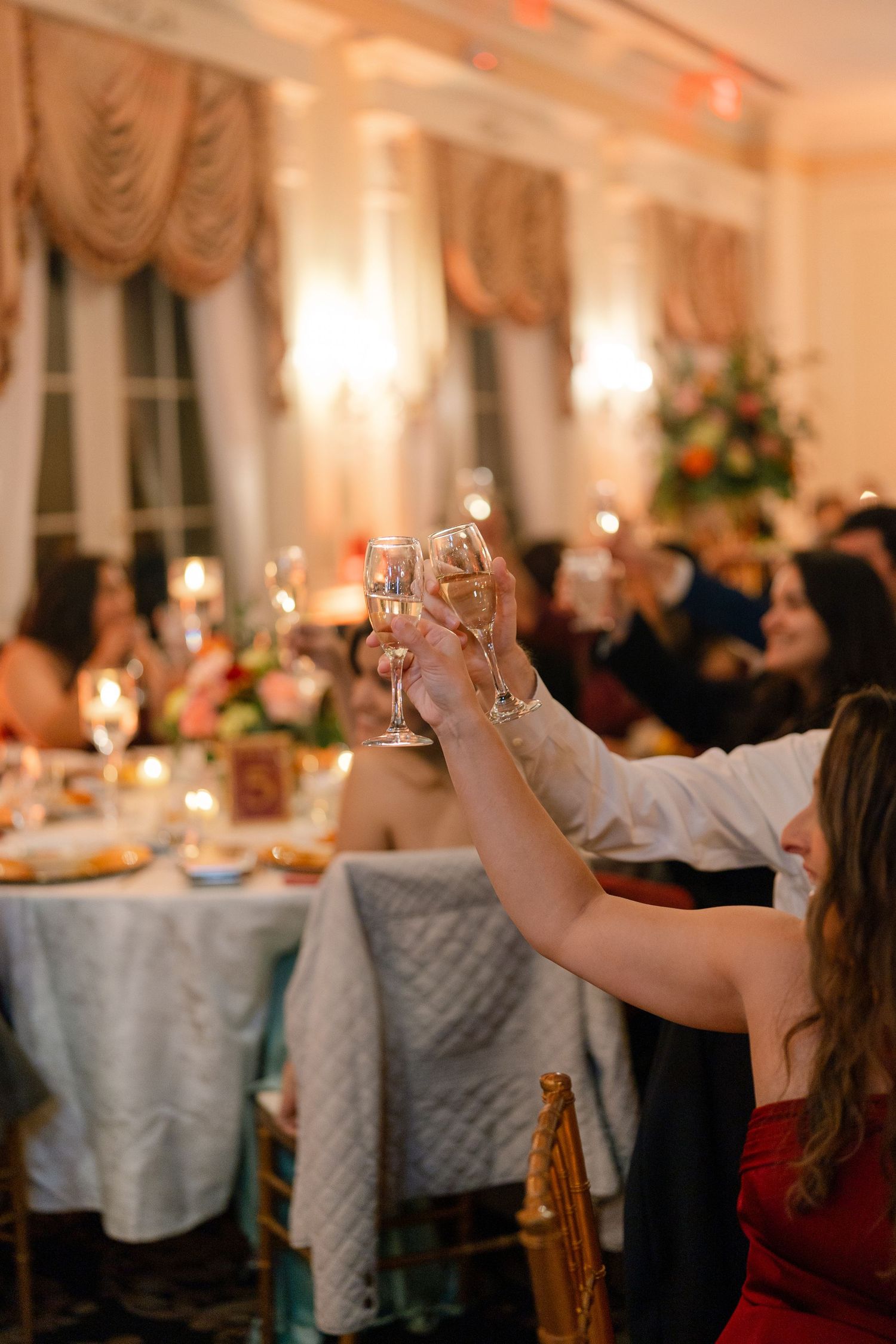 Wedding reception venue with elegant table settings and guests raising glasses in a toast.