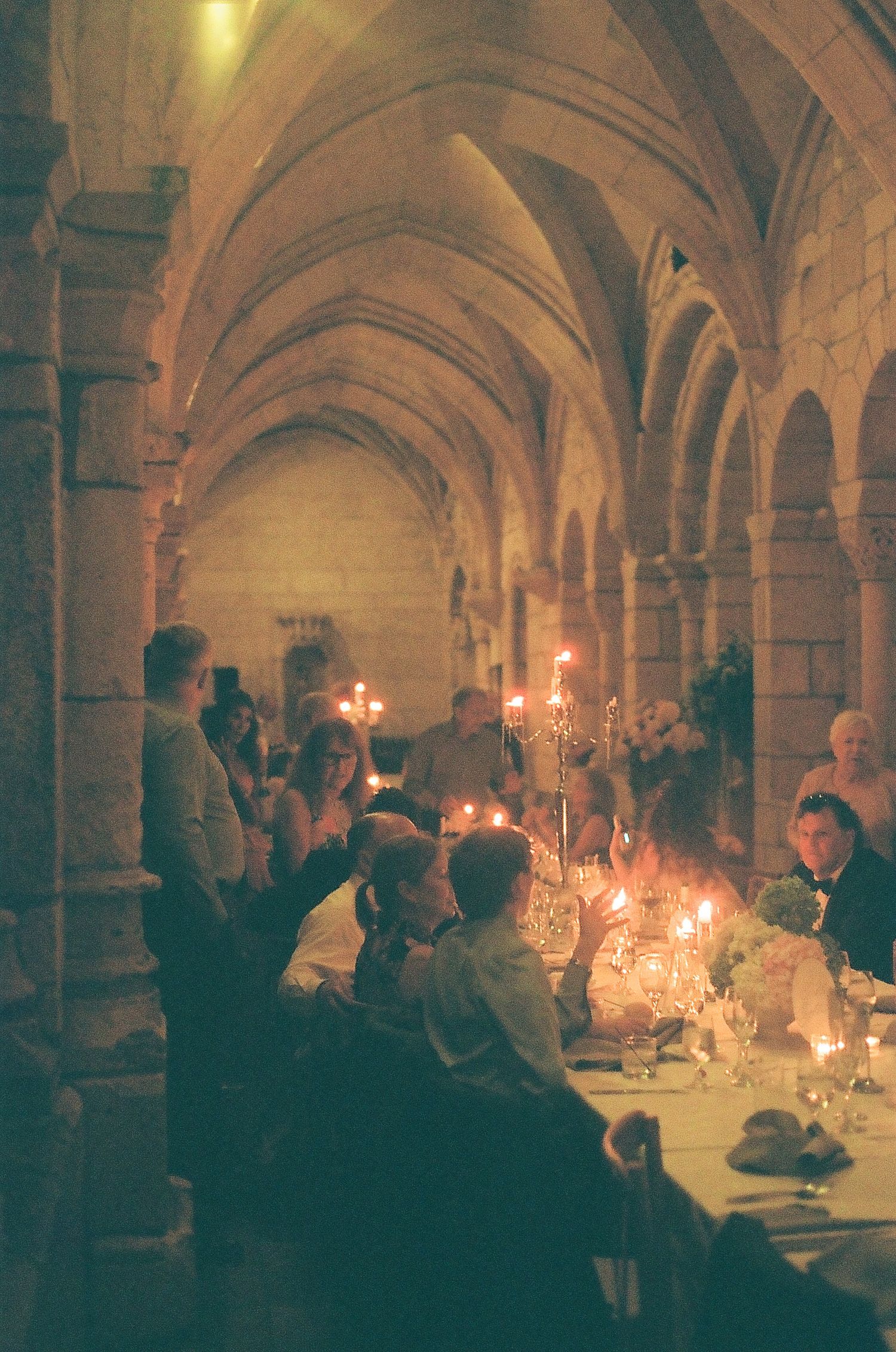 Romantic candlelit wedding reception dinner in historic stone vaulted hall with arched ceilings.