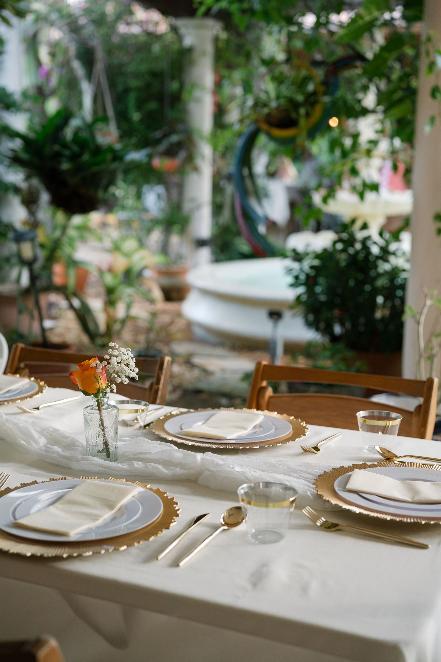 Elegant table setting with gold-rimmed plates and white linens in an outdoor setting.
