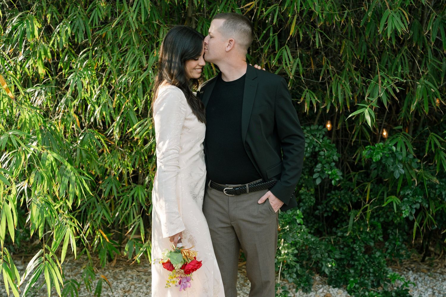 Romantic moment captured against lush bamboo garden backdrop with floral bouquet.