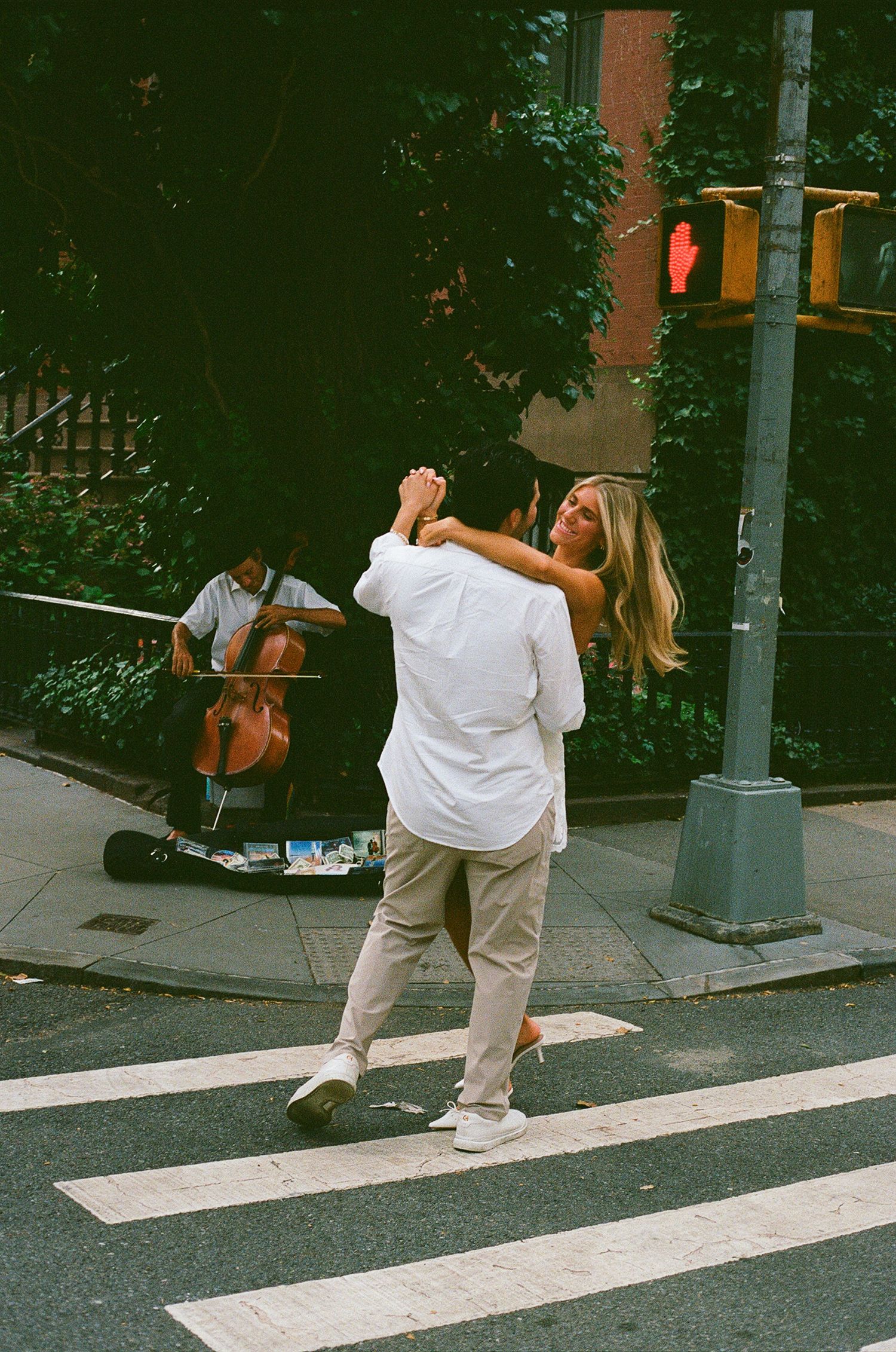 Couple dancing on a crosswalk in NYC while a street musician plays cello in the background.
