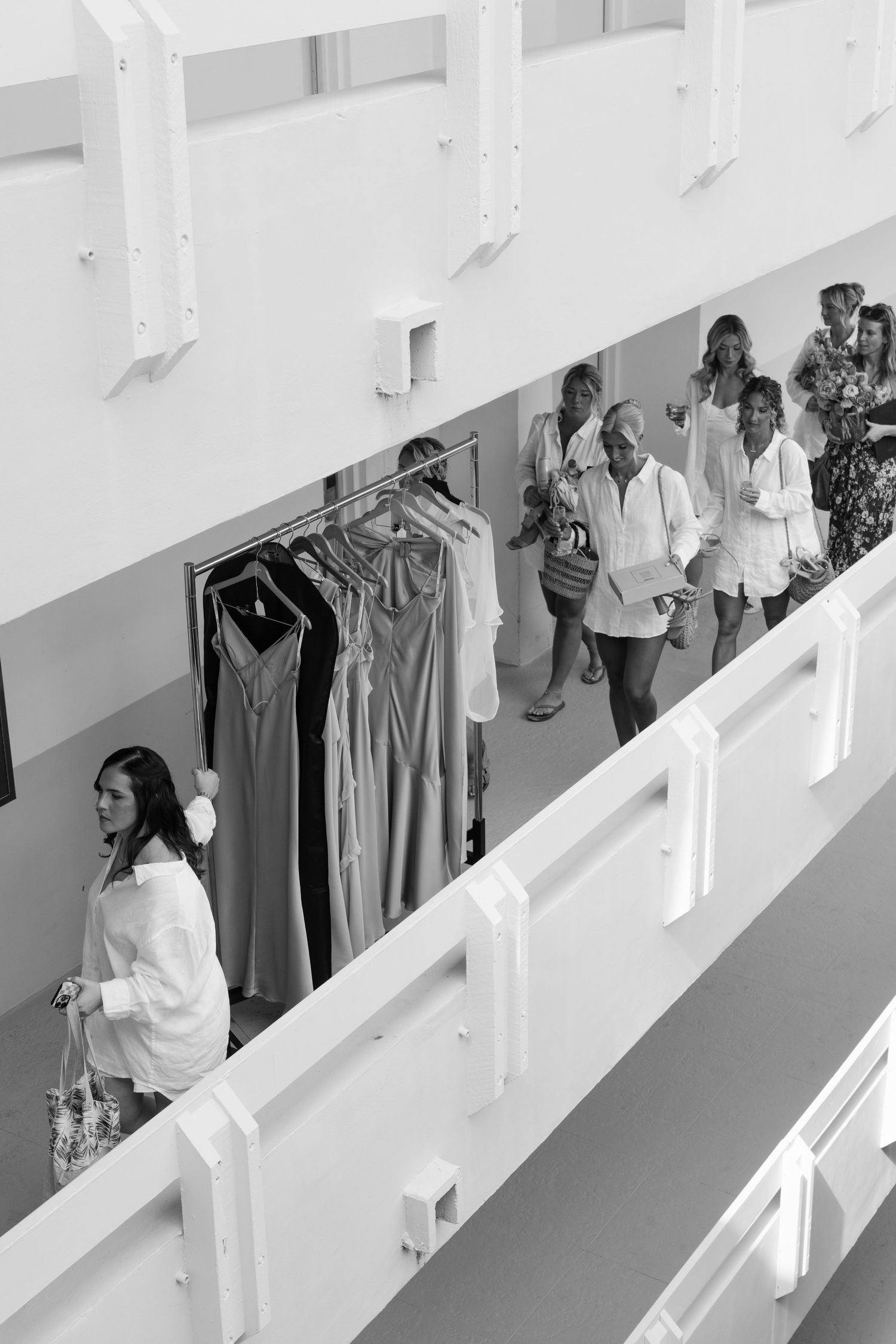 Black and white photo showing clothing racks and people walking along a balcony hallway.