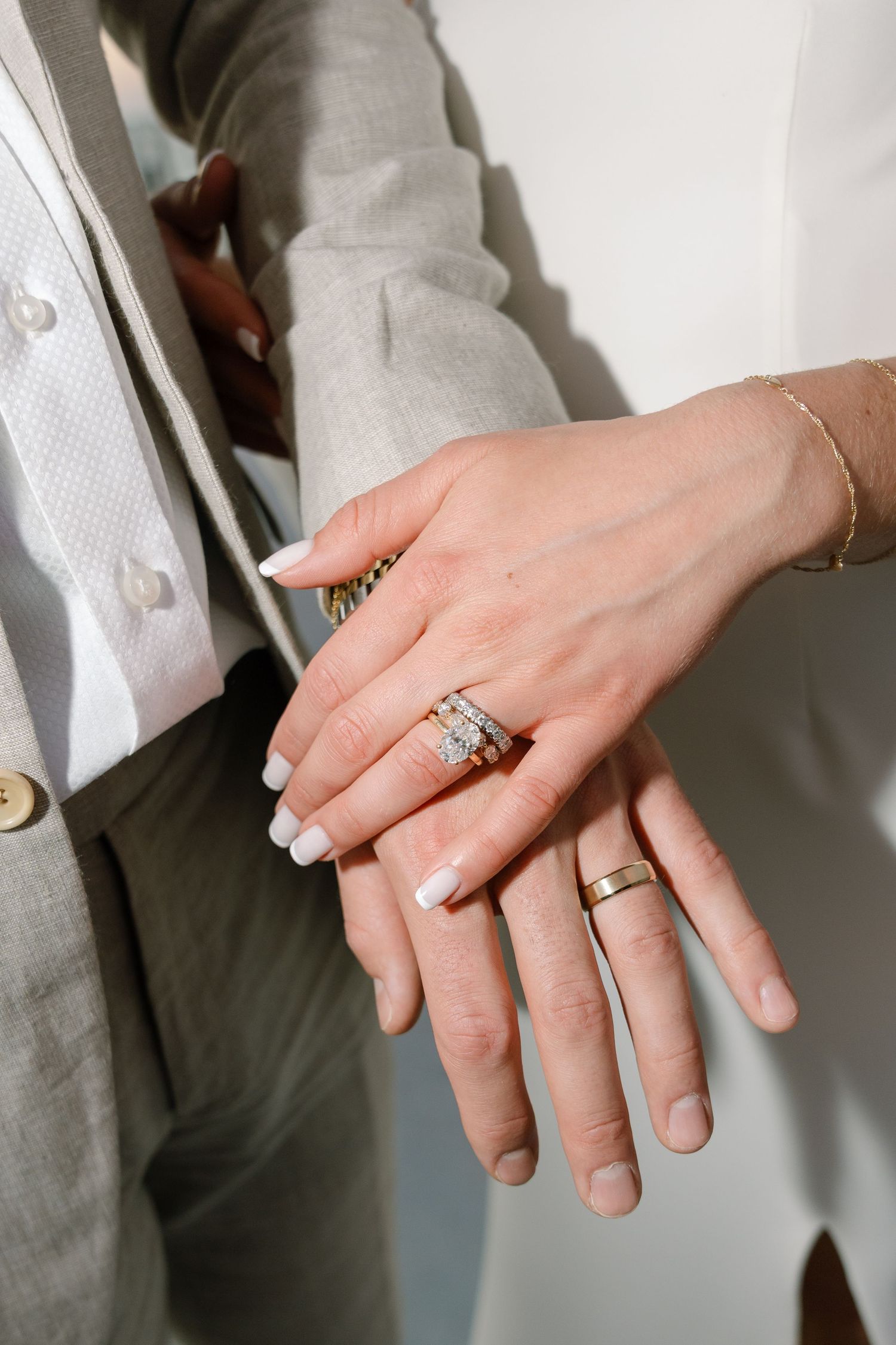 Close-up of wedding rings and jewelry on hands showing intricate details.