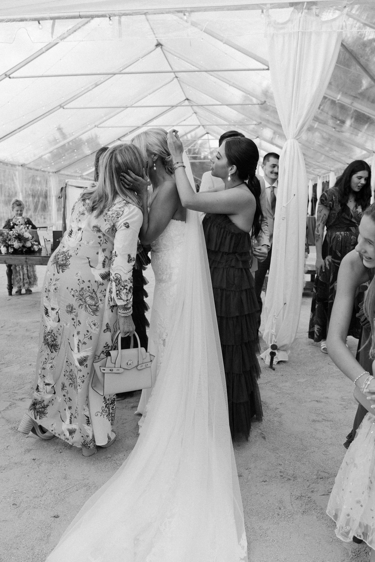 Wedding guests embrace under a white tent during reception celebrations.