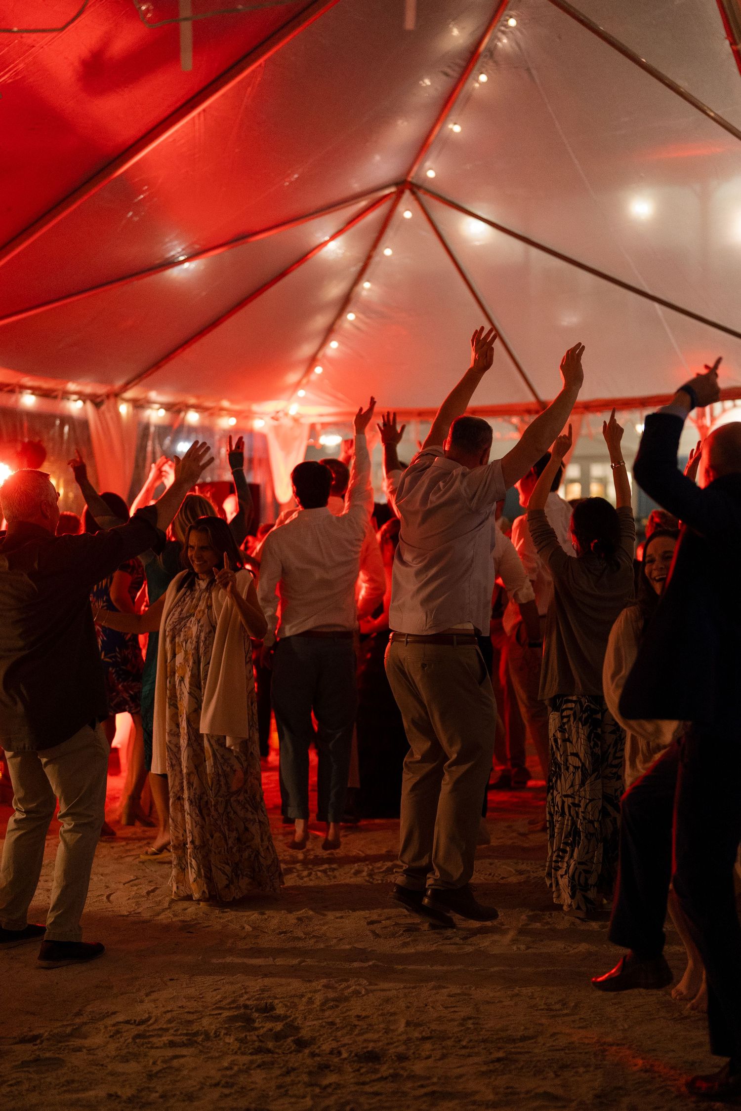 Silhouettes of people dancing under a red-lit tent canopy at an evening celebration.