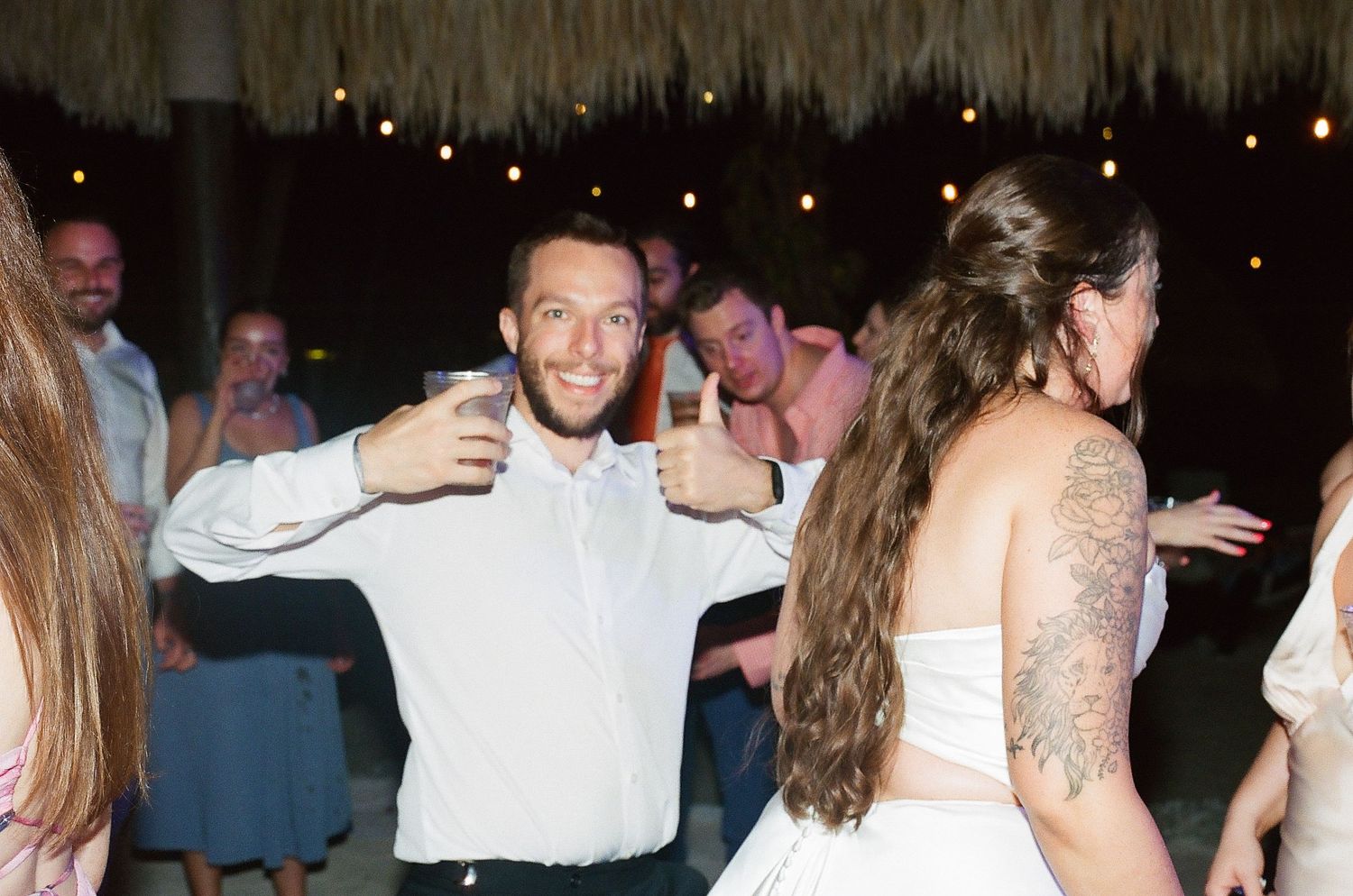 Guests dancing and celebrating at an outdoor tropical wedding reception under string lights at night.