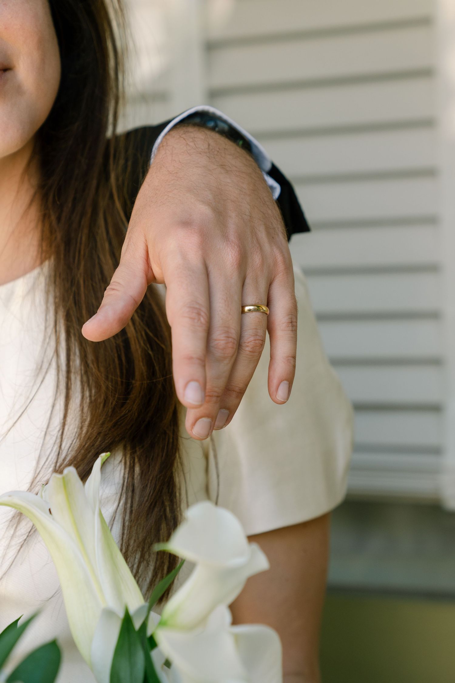 Close-up shot of hands holding elegant white lilies against a light background.