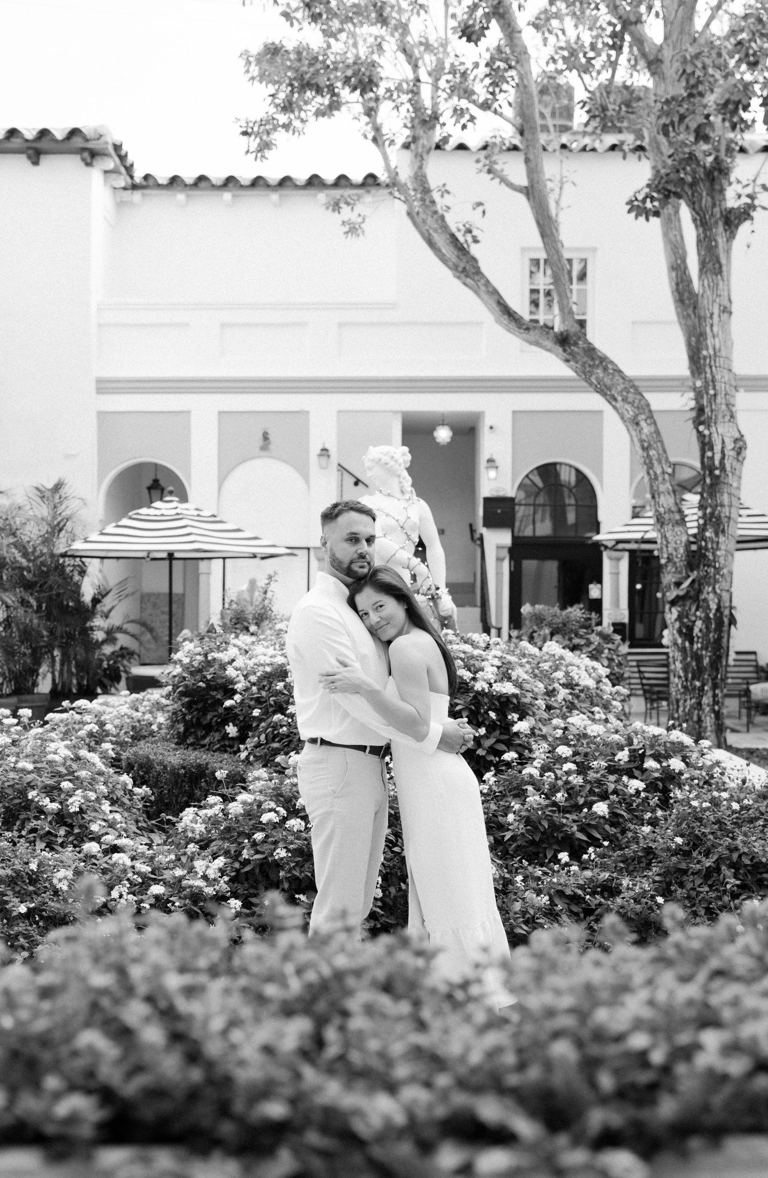 A romantic black and white photo sequence of a couple dancing together in a garden with white Spanish-style architecture.