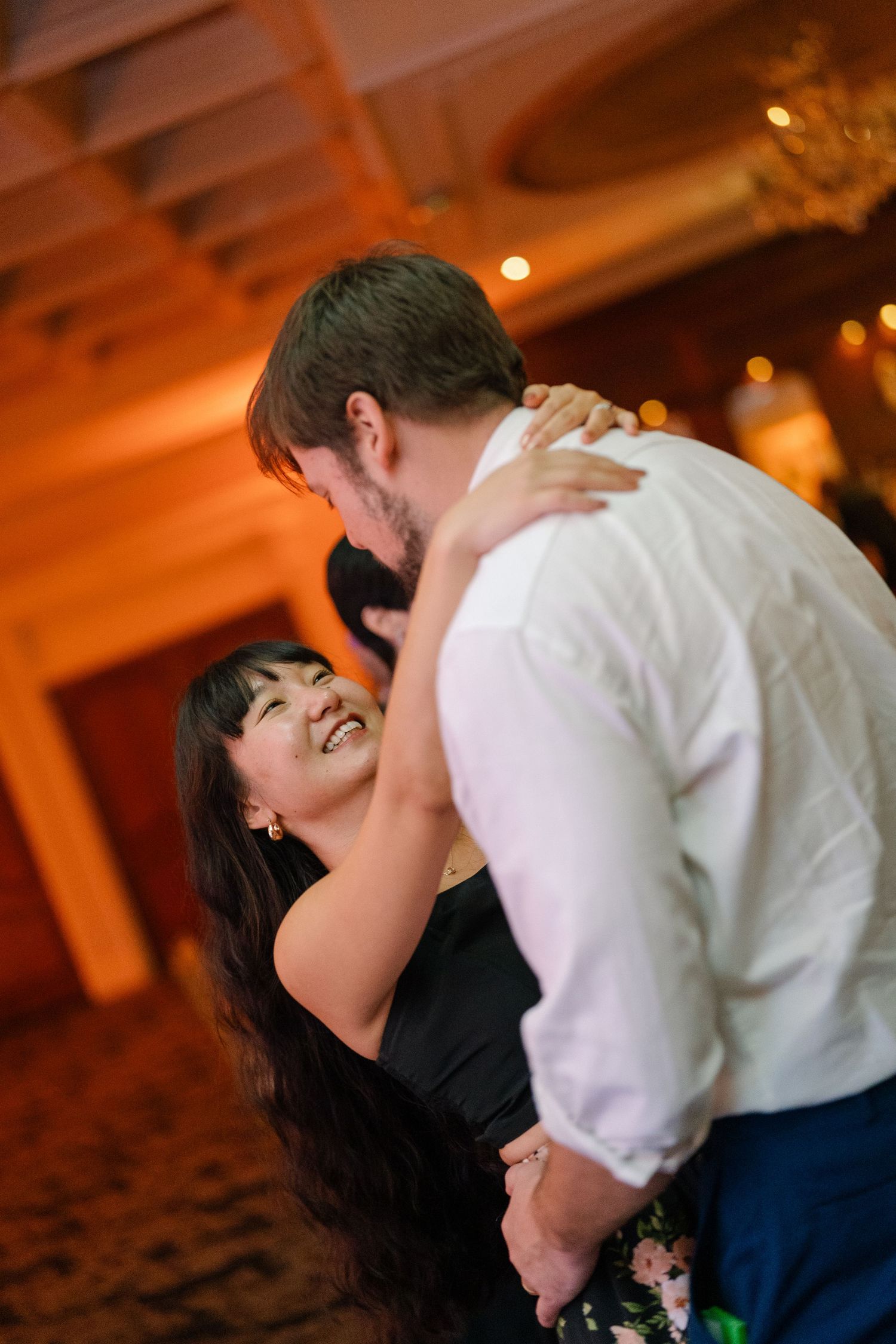 A romantic couple shares a passionate kiss in a warmly lit indoor venue with orange ambient lighting.