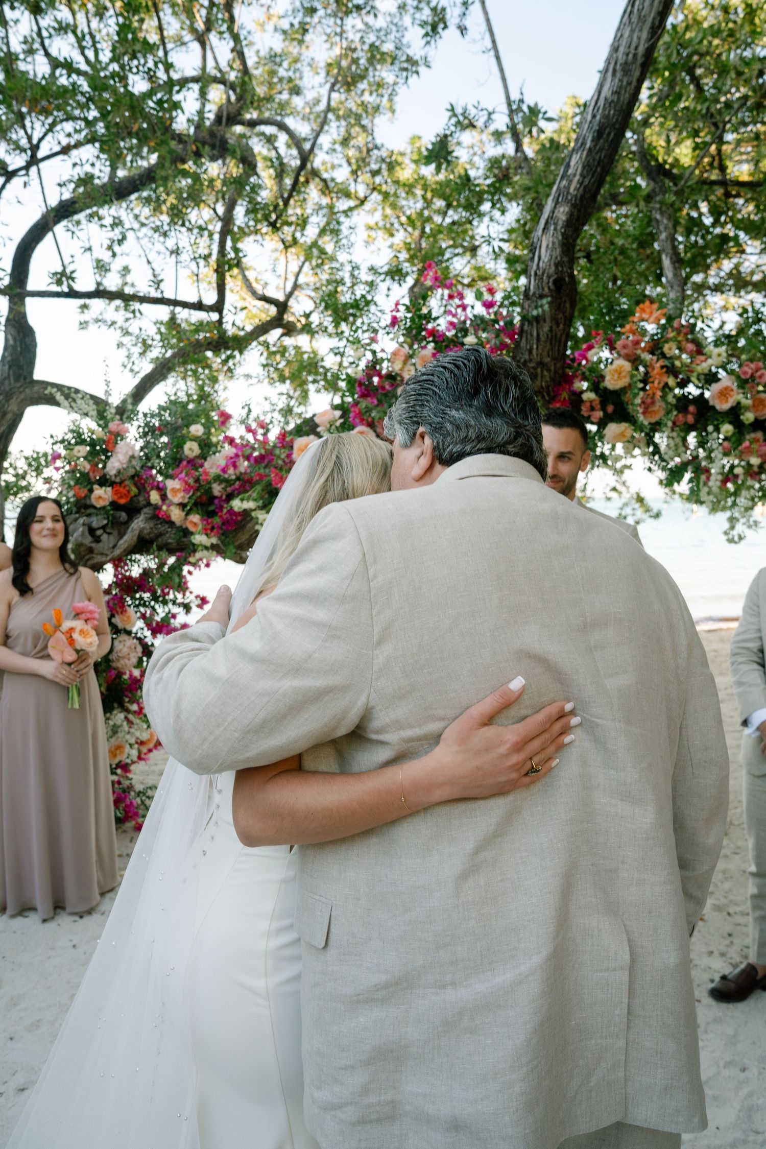Wedding couple embracing under flowering trees with pink blossoms at an outdoor ceremony.