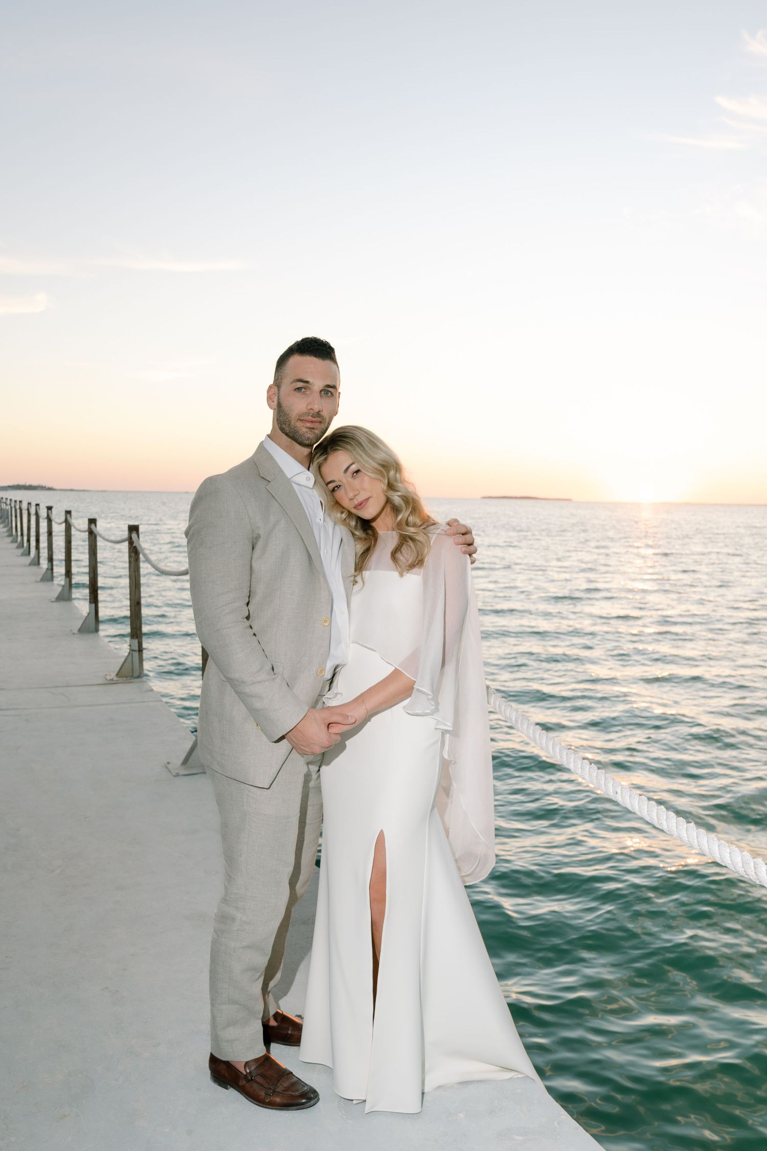 Romantic sunset photos of a couple on a pier overlooking turquoise waters.