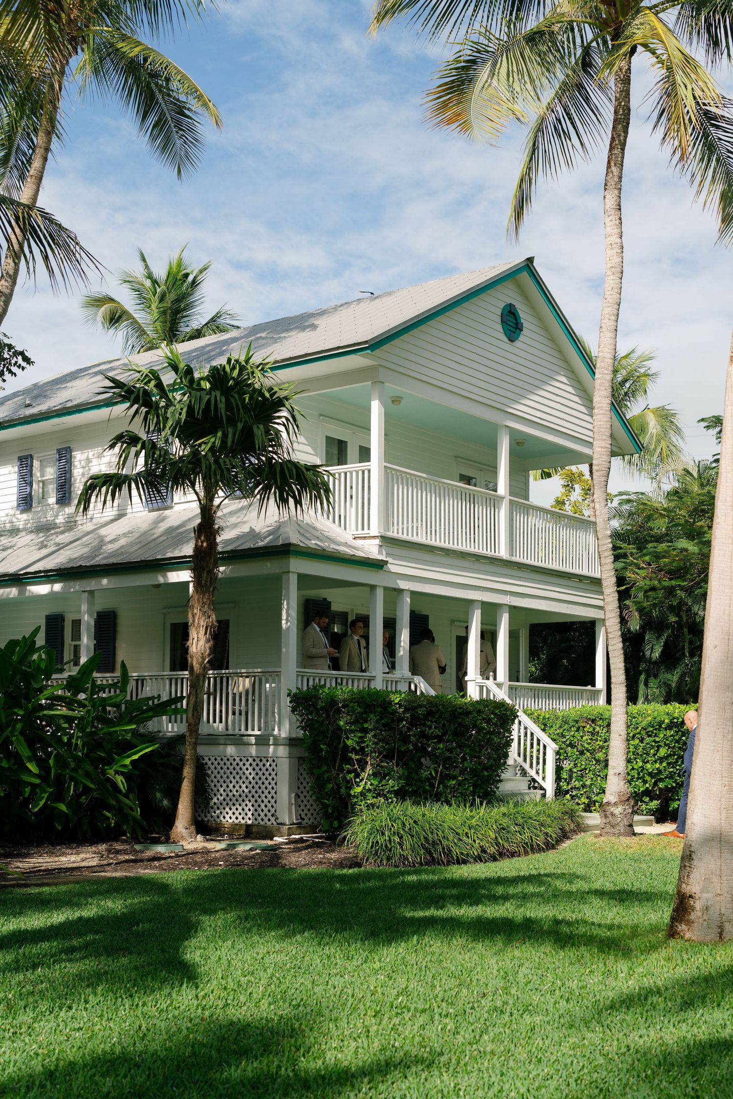 Row of elegant white beach houses with green roofs surrounded by palm trees and manicured lawns.