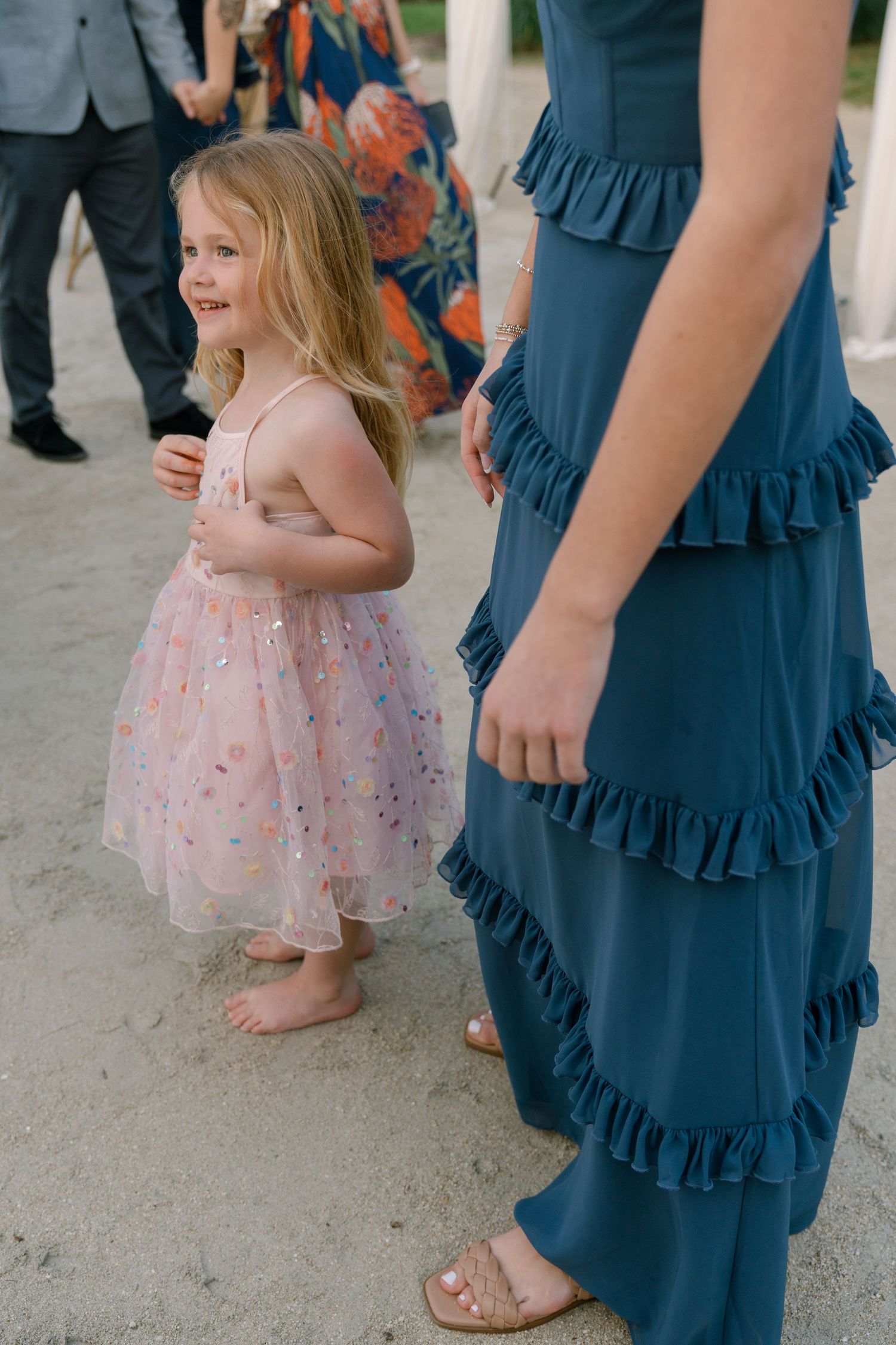 A young girl in a pink dress dances next to someone wearing a blue ruffled dress at a wedding.