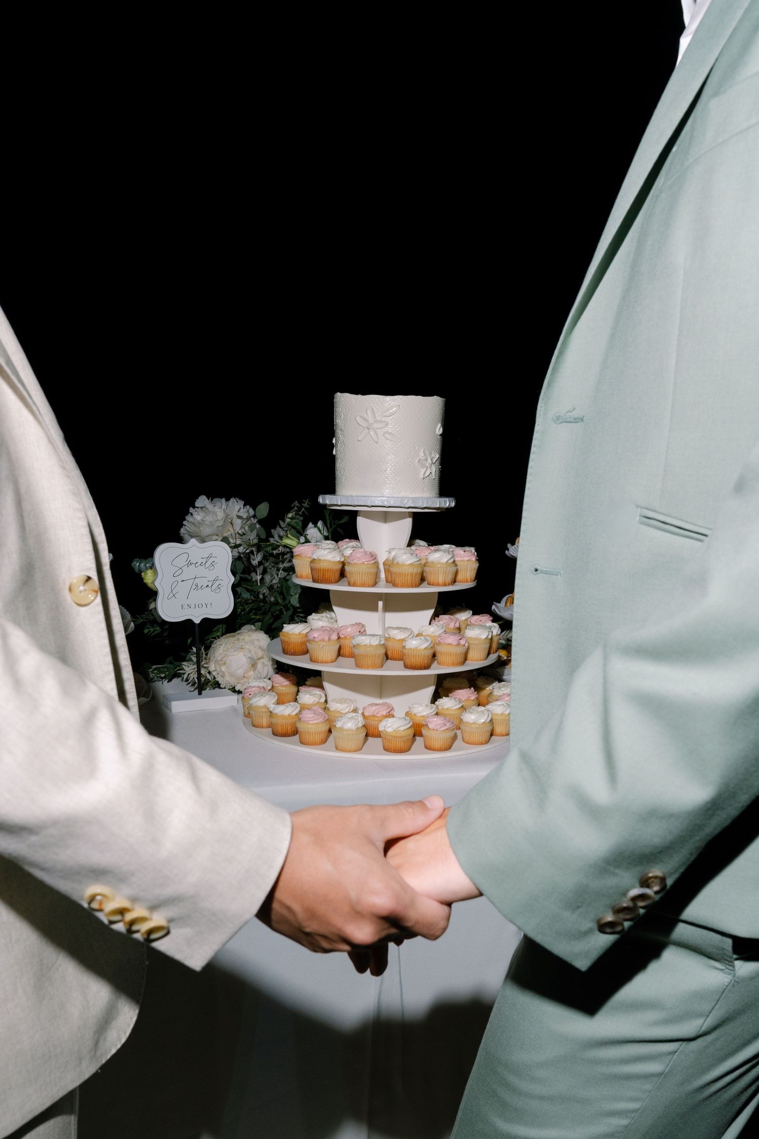 Wedding couple cutting cake together while holding hands in formal attire at reception.