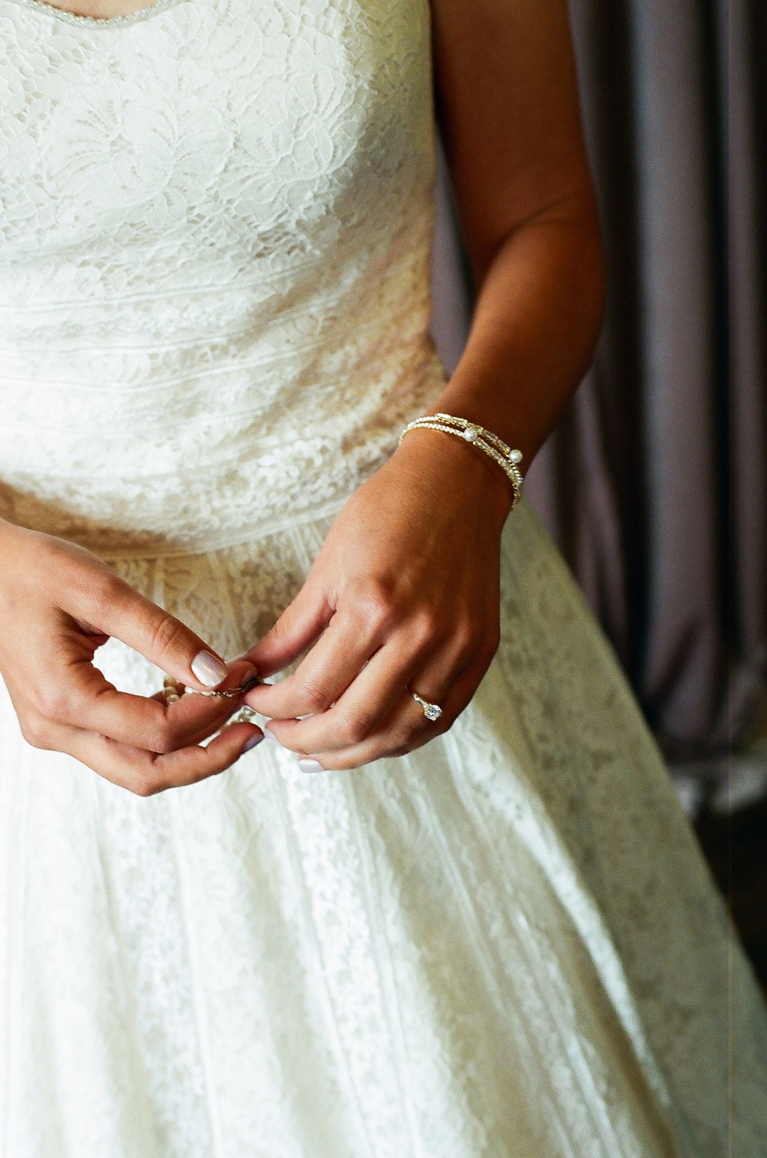 Close-up details of lace on a white wedding dress with a gloved hand making adjustments.