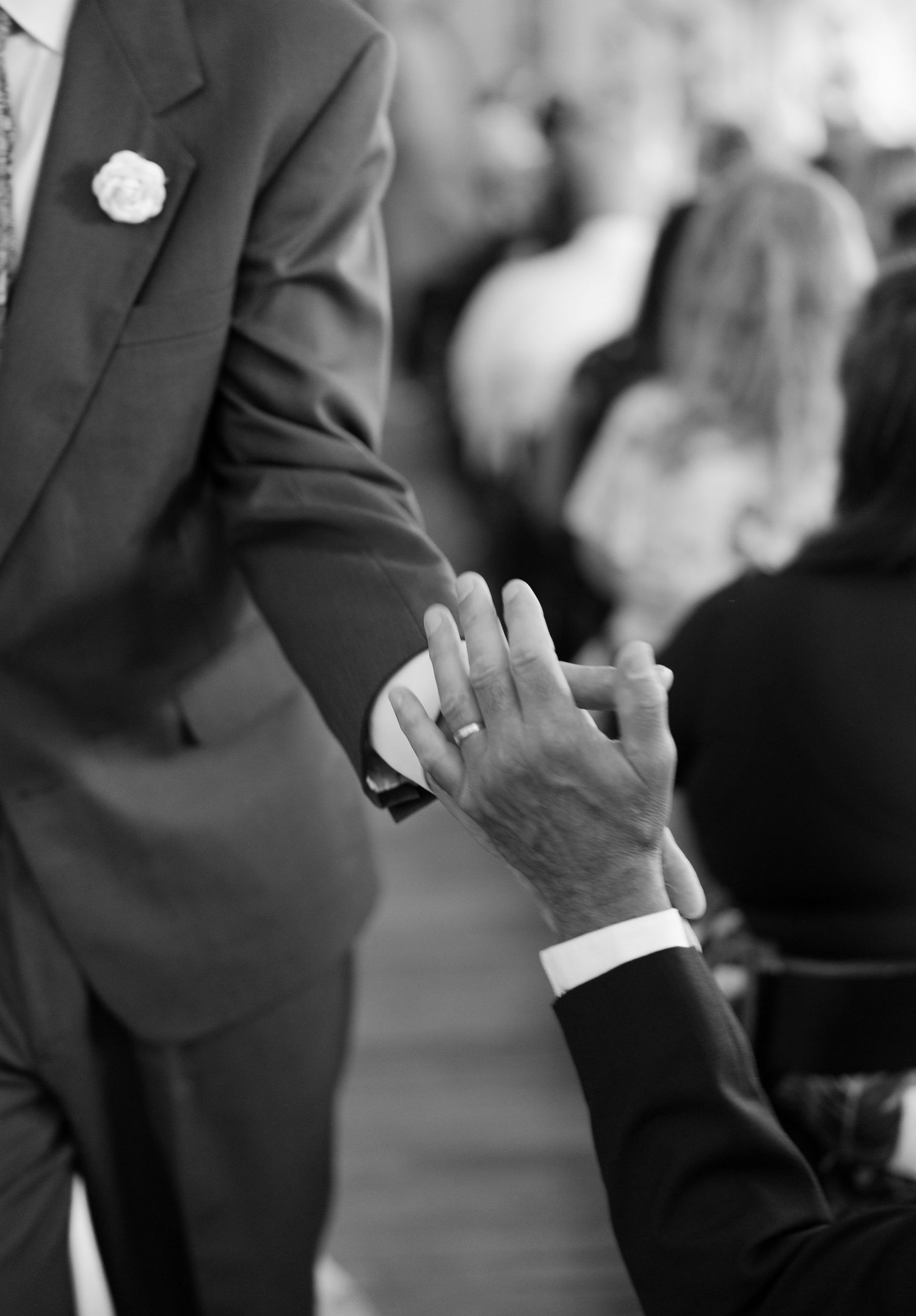 Close-up black and white photo of hands wearing wedding rings at a formal ceremony.