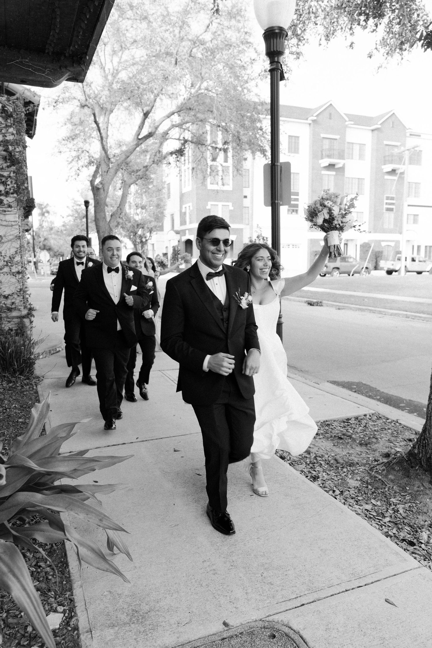 Wedding party walking along autumn sidewalk in black and white photograph.