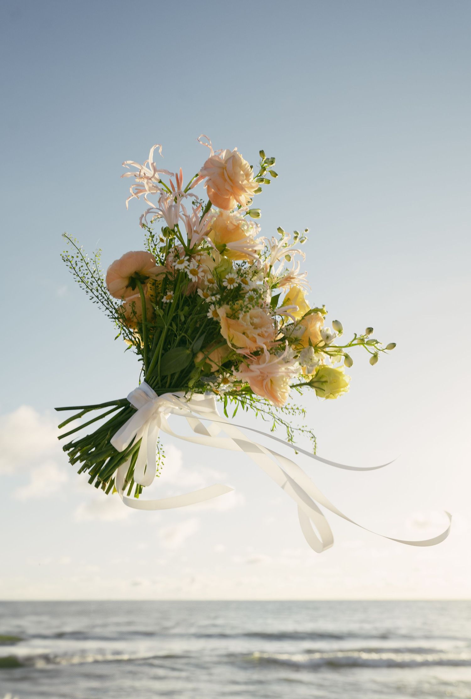 Delicate peach and white floral wedding bouquet floating against a sky background.