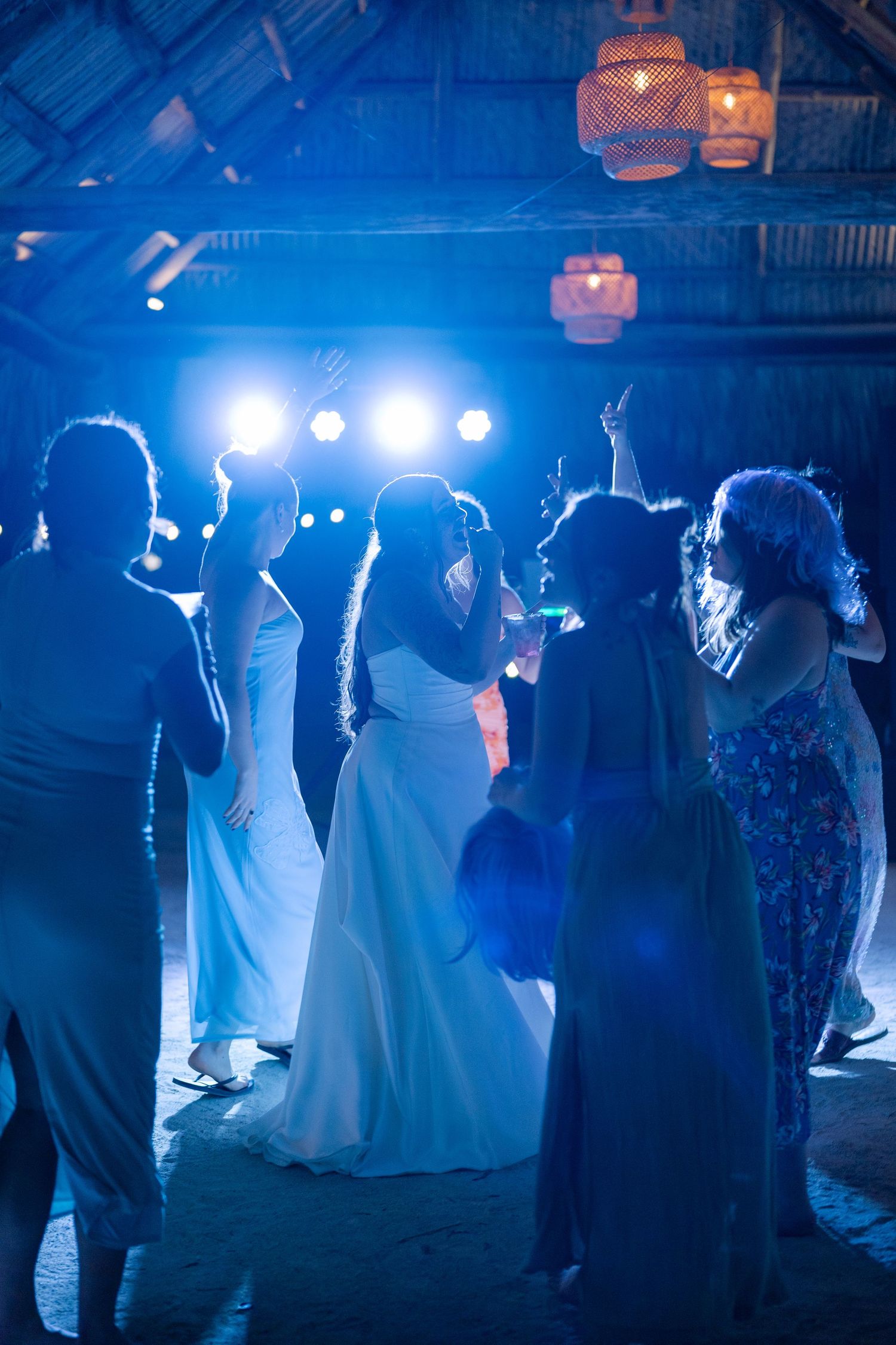 A group of people dancing at a dimly lit event with colorful lighting and lanterns hanging overhead.