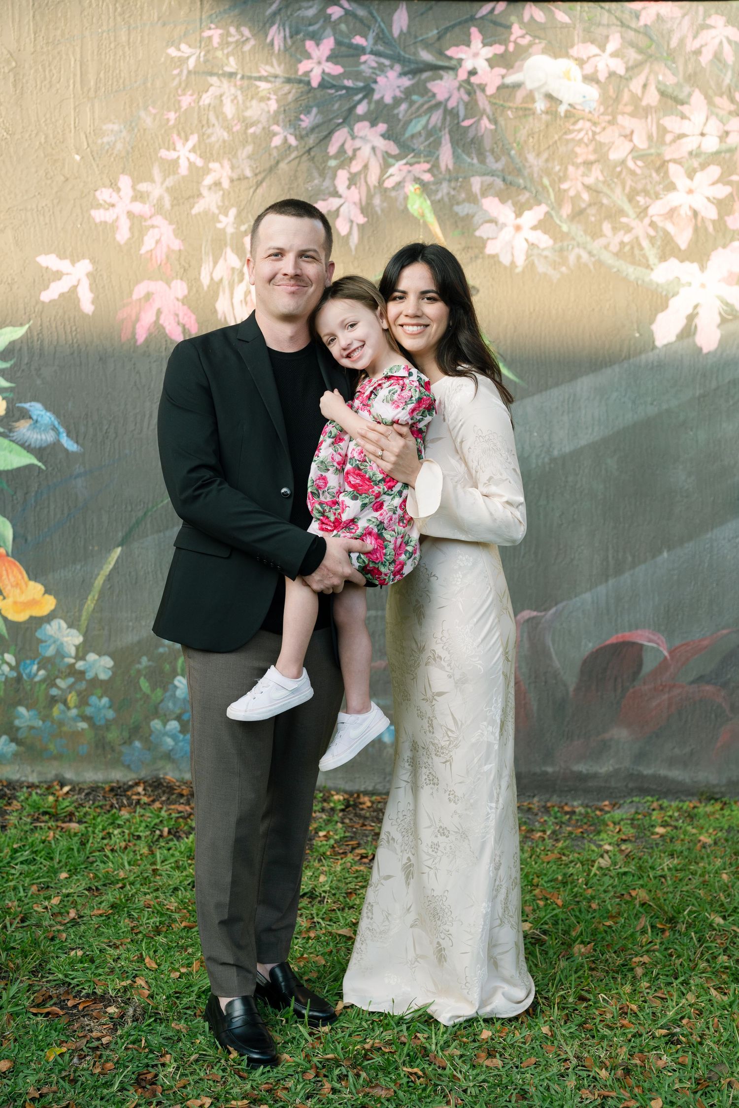 A family poses against a floral mural backdrop in formal attire.