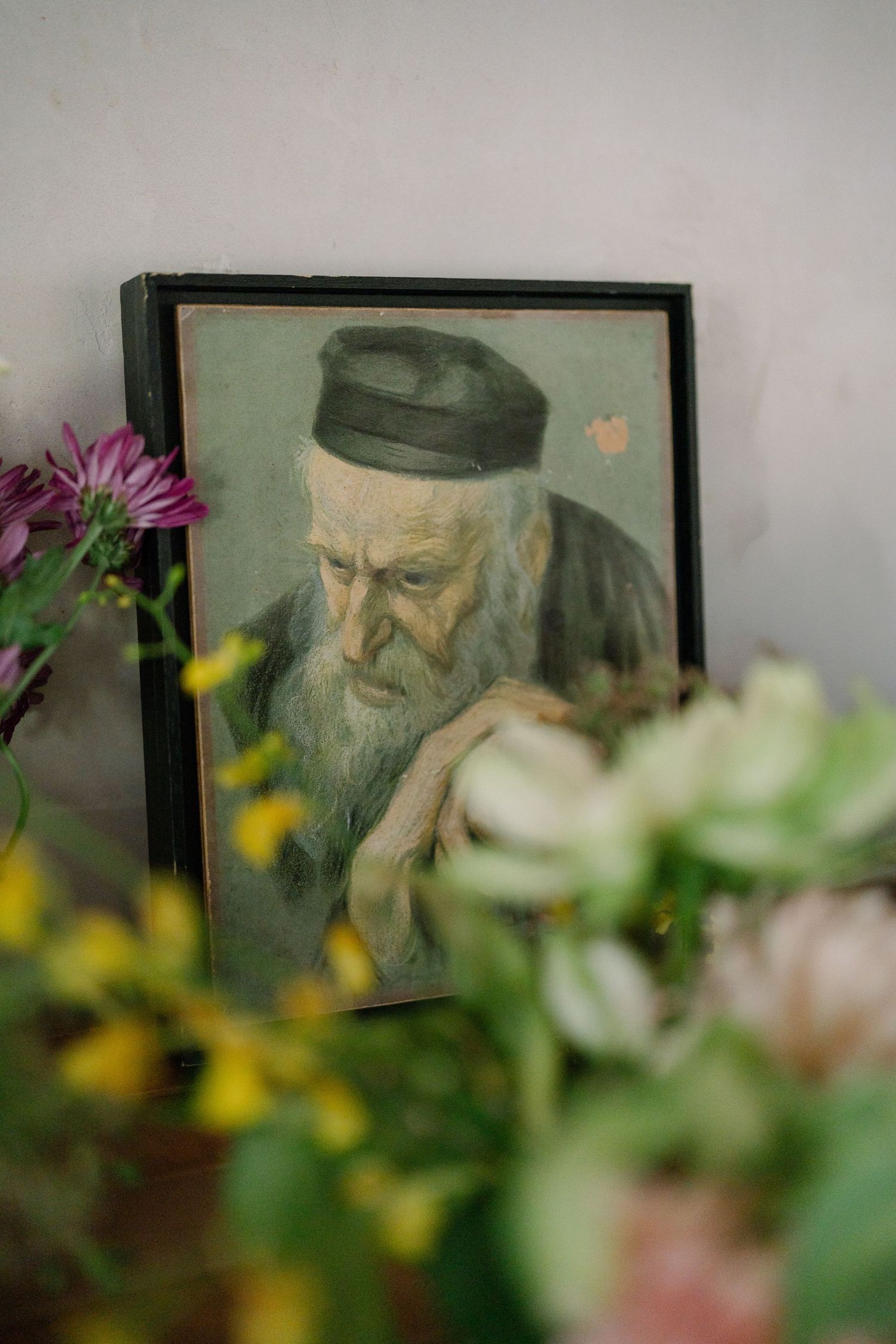 A framed portrait sits among soft-focus flowers and greenery in a dreamy, artistic composition.