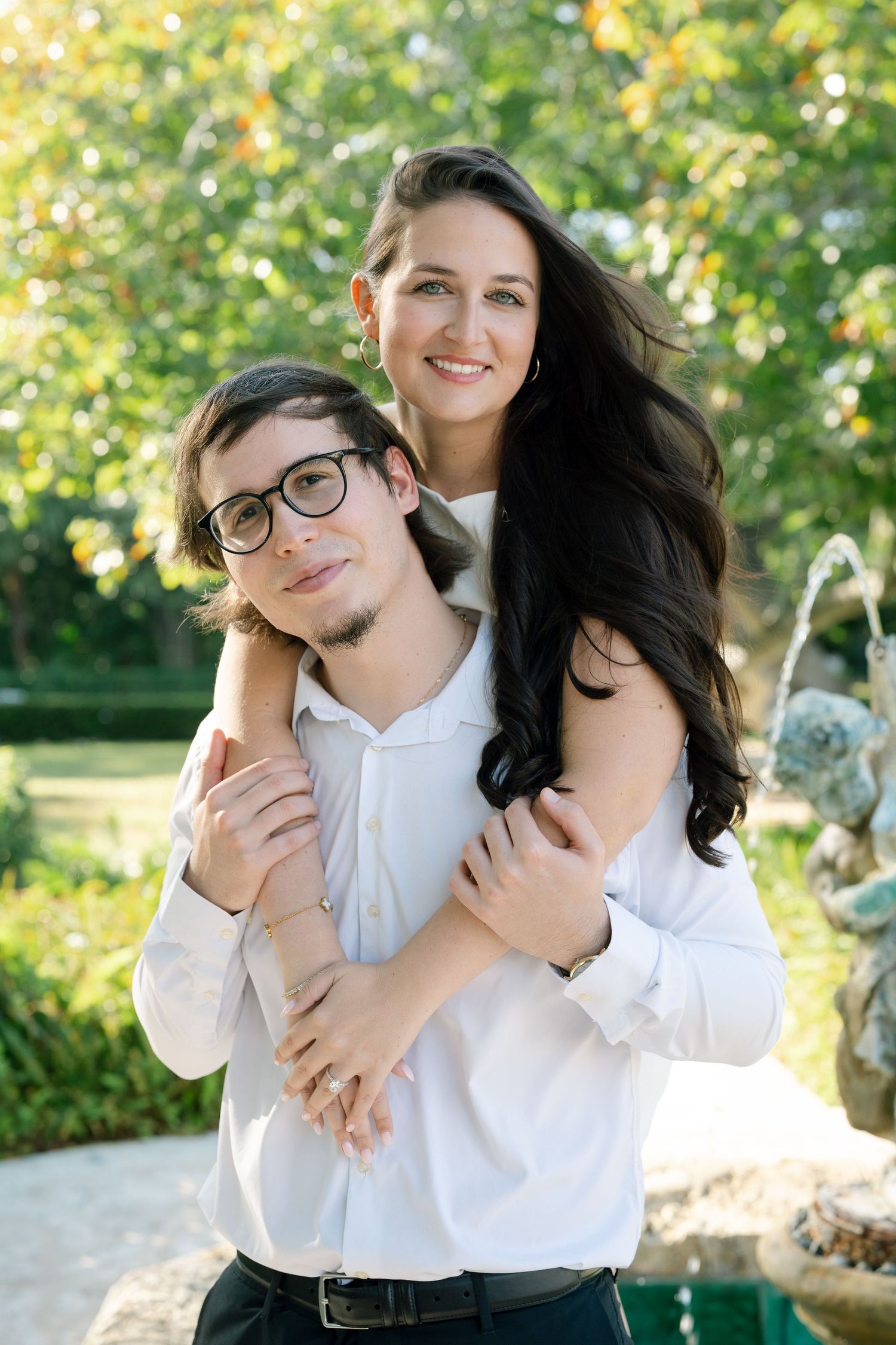 Couple in white shirts embracing and laughing together in a sunny garden setting.