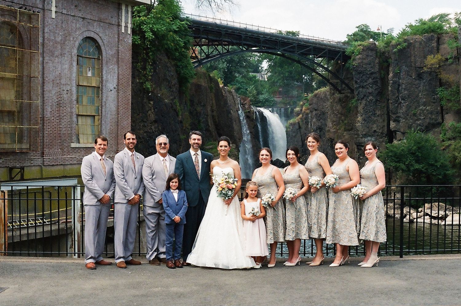 Wedding party in neutral colors poses together on stone steps during outdoor celebration.